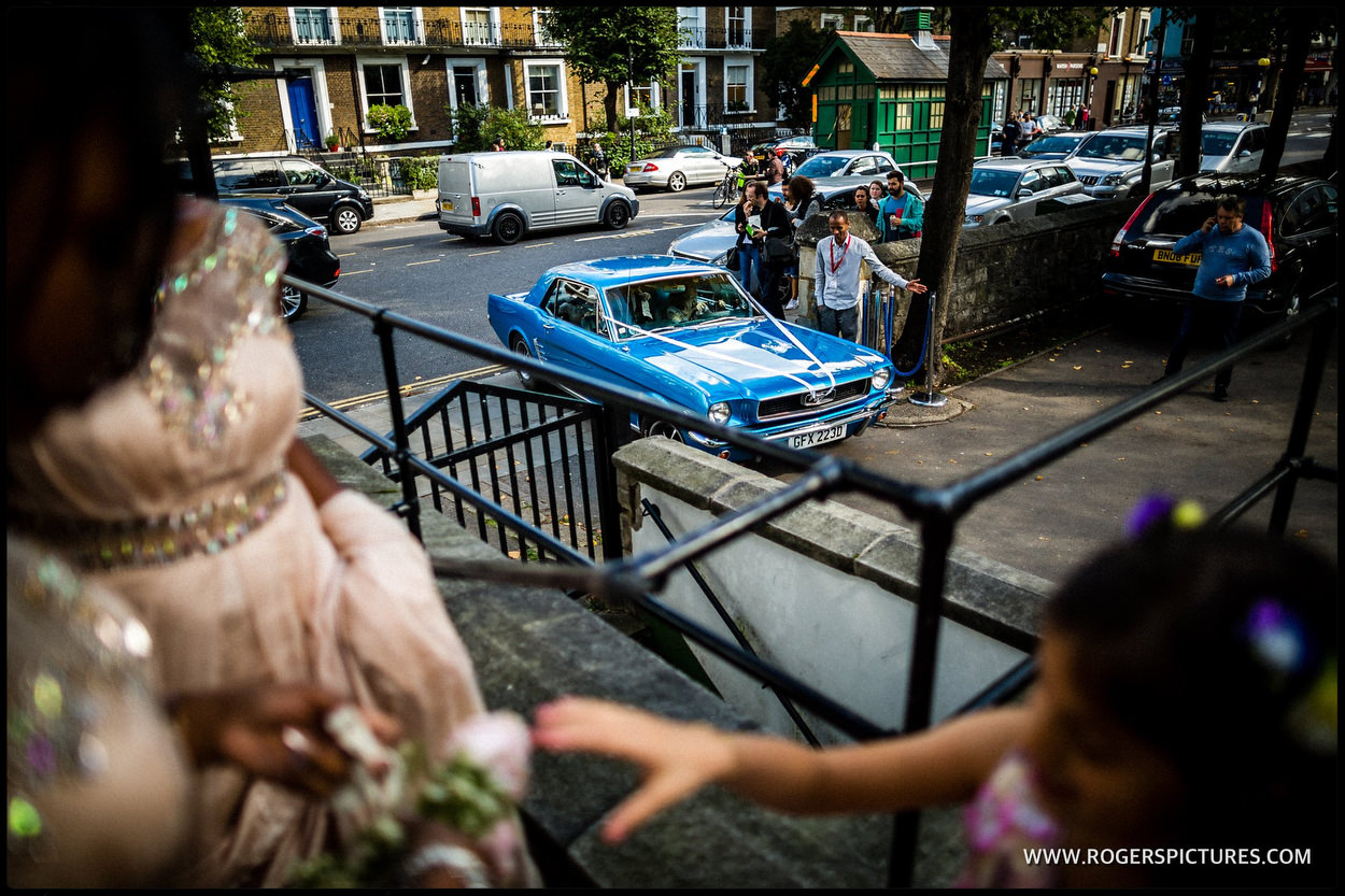 Bride arrives at Kensington Temple in a blue Mustang wedding car
