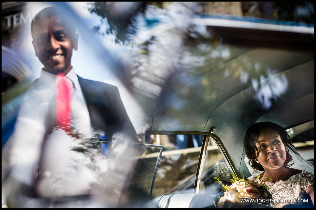 Bride sitting in the wedding car, groom reflected in the window
