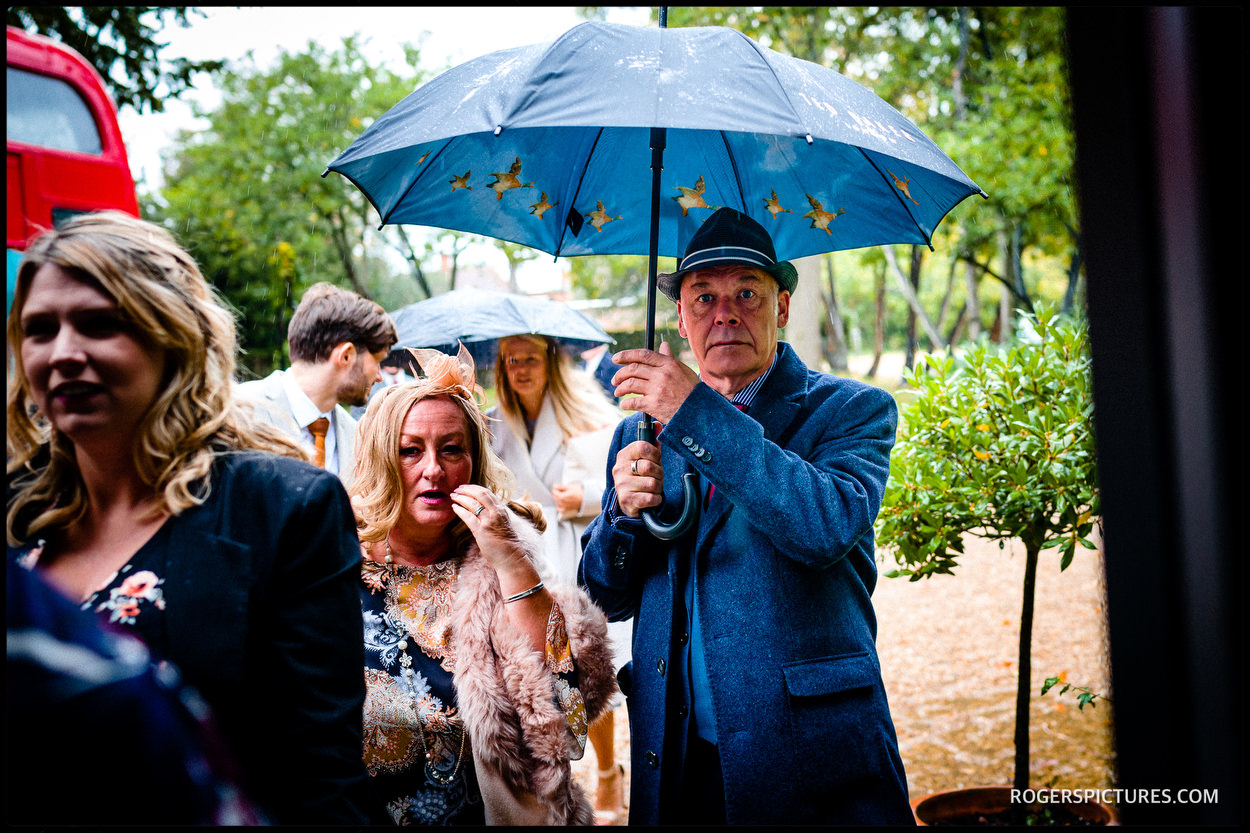 Guests with umbrellas at a wedding at Stoke Place Hotel in Buckinghamshire