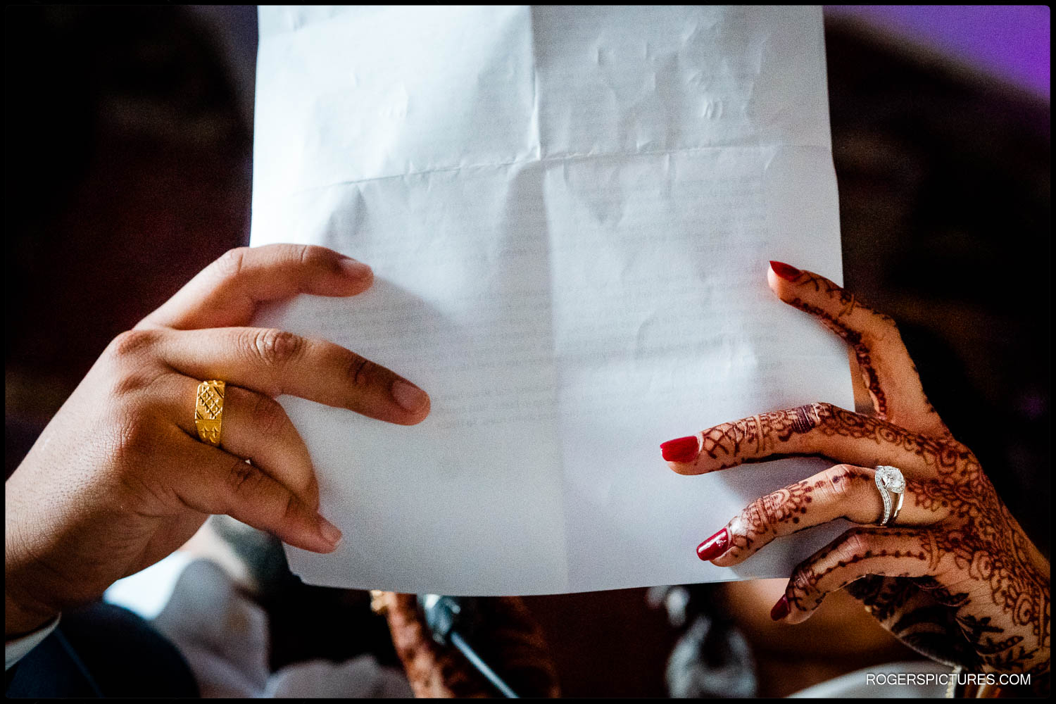 Photo of brides hand with henna and grooms hand holding a wedding speedh