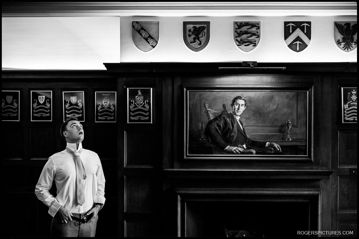 Groom Getting Ready at Gray’s Inn – A black and white image of the groom adjusting his tie in a wood-paneled room, under a portrait of a historic figure.