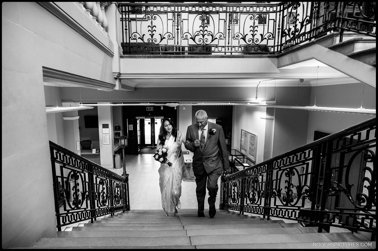 Bride walking up the grand staircase of Hendon Town Hall with her father, ready for the wedding ceremony.