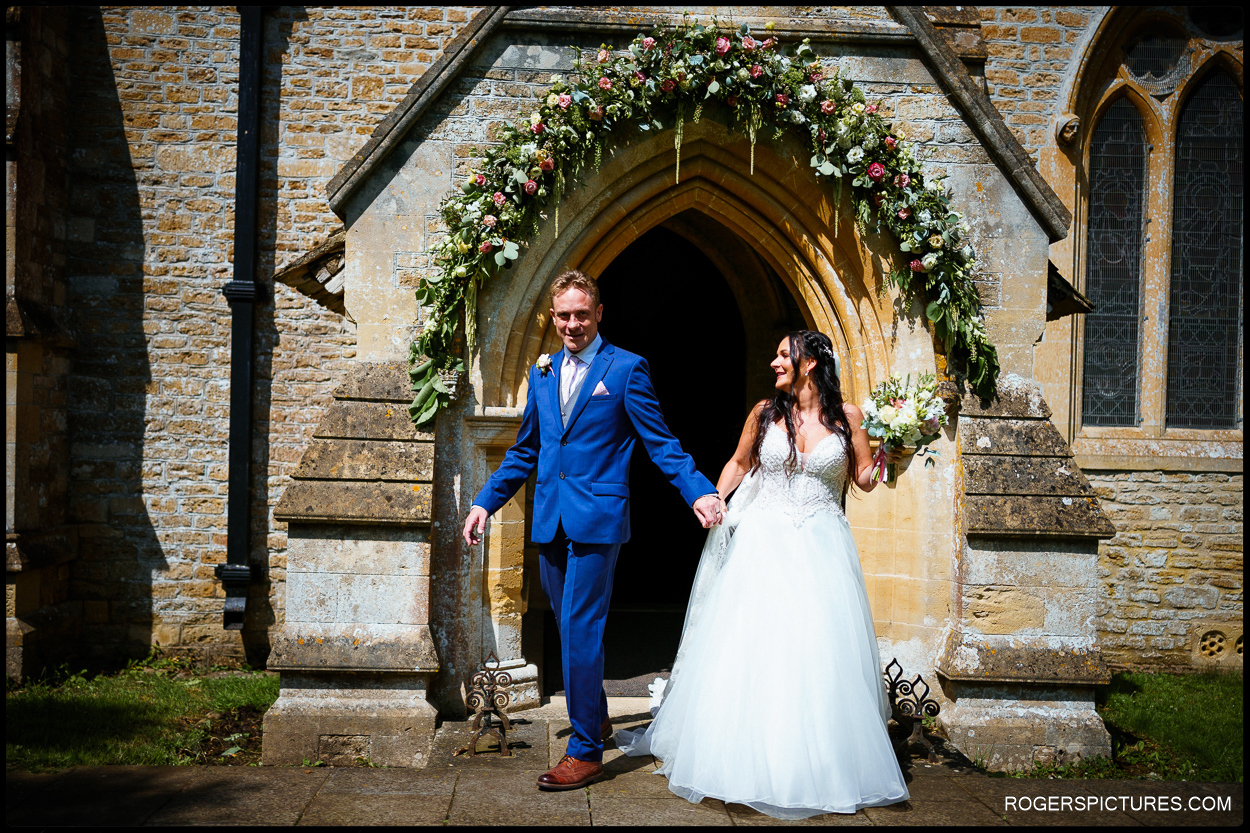 Newlywed couple exit church after summer wedding at Orchardleigh House