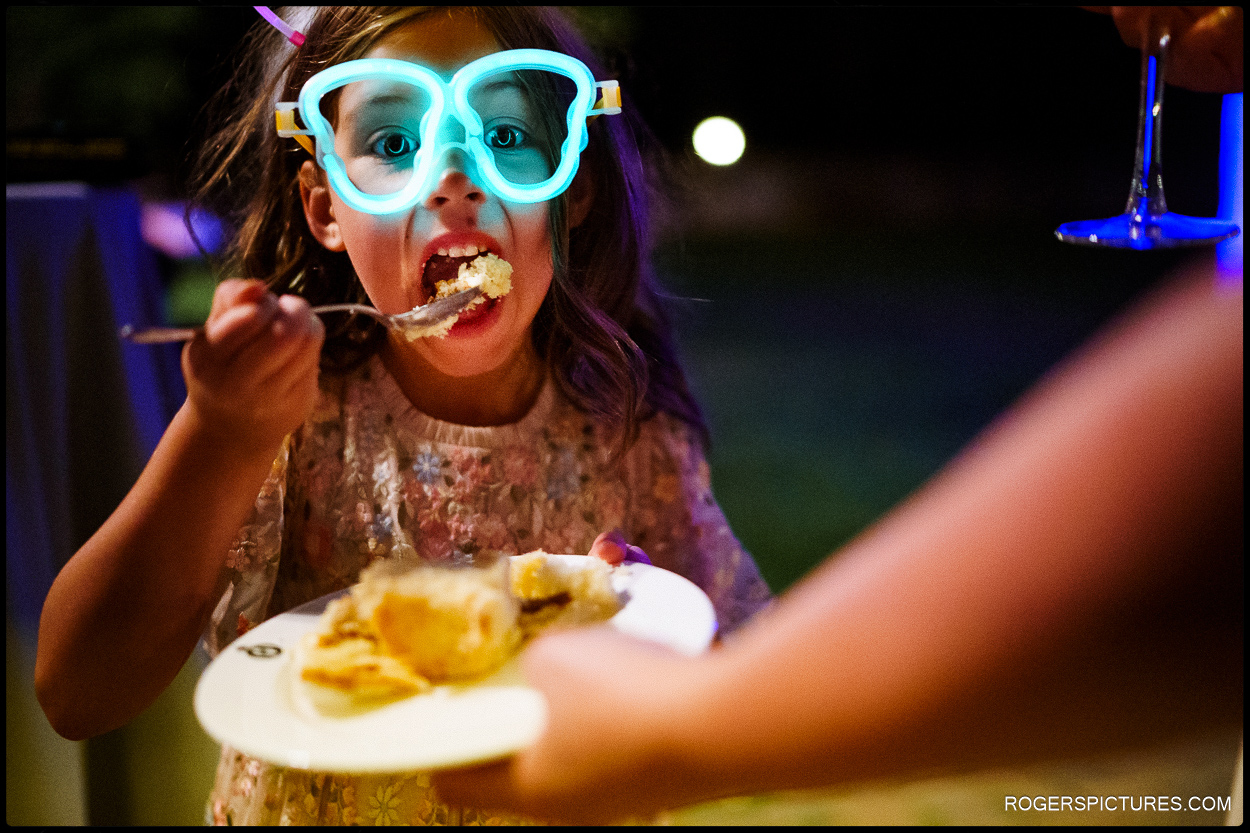 Photo of a girl in illuminated glasses eating wedding cake at a destination wedding in Spain