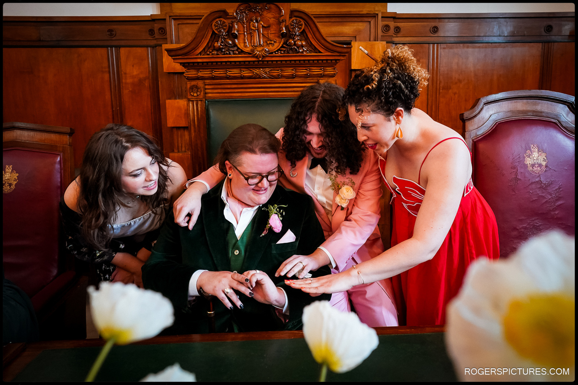 London Wedding at Town Hall Hotel – Friends gather around the grooms, admiring the wedding rings in a joyful post-ceremony moment.