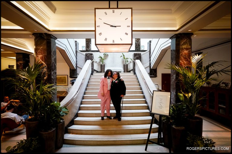 London Wedding at Town Hall Hotel - The couple stands together at the grand staircase of the Town Hall Hotel, framed by elegant Art Deco interiors.