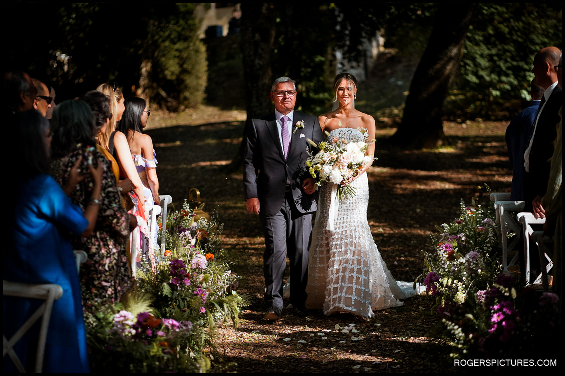 Bride and Father Arriving at the Ceremony – A proud father walks his daughter down a beautifully adorned woodland aisle, guests watching with admiration.