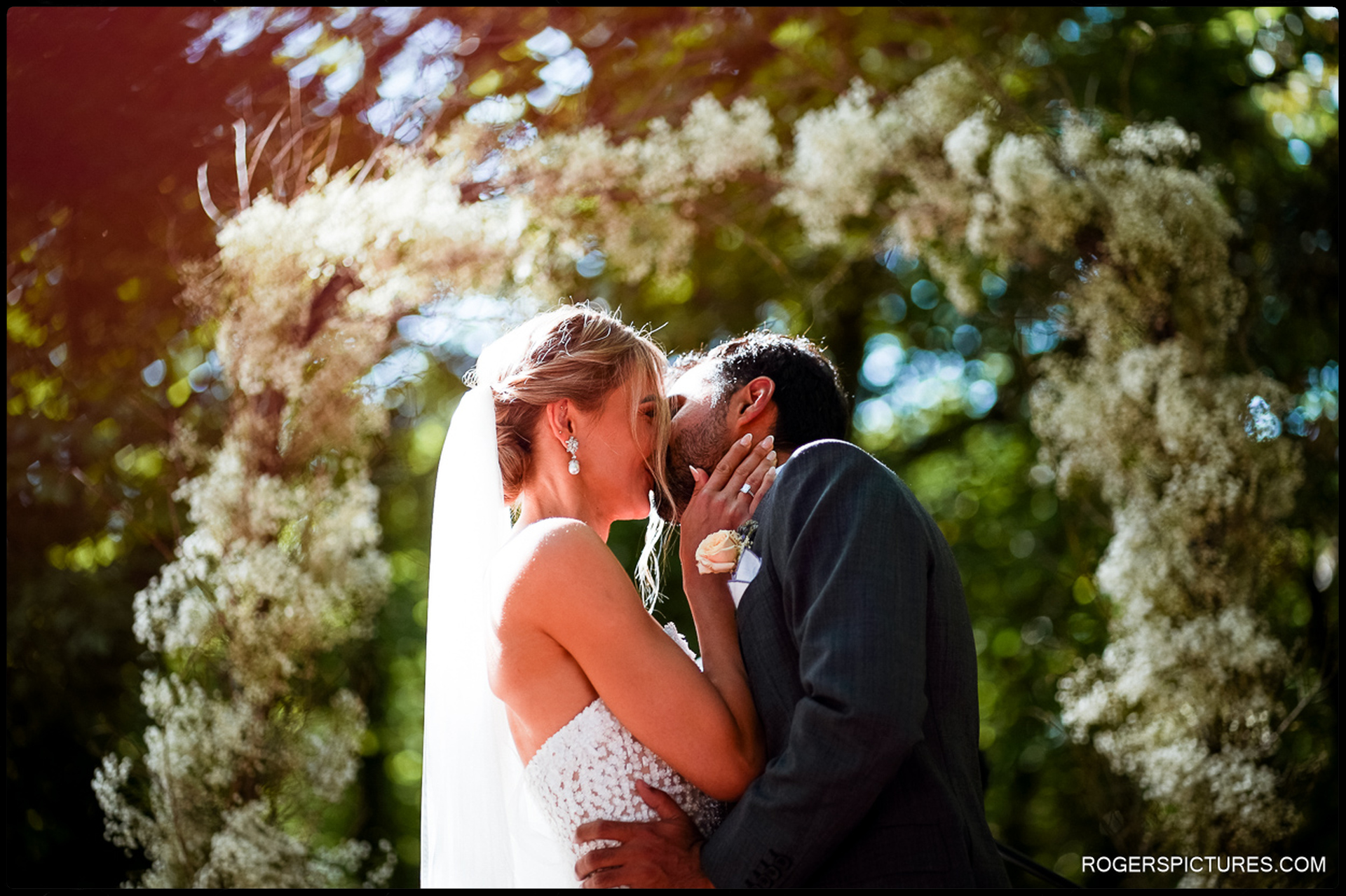 Bride and groom kiss beneath a floral arch in a woodland wedding ceremony in Tuscany.