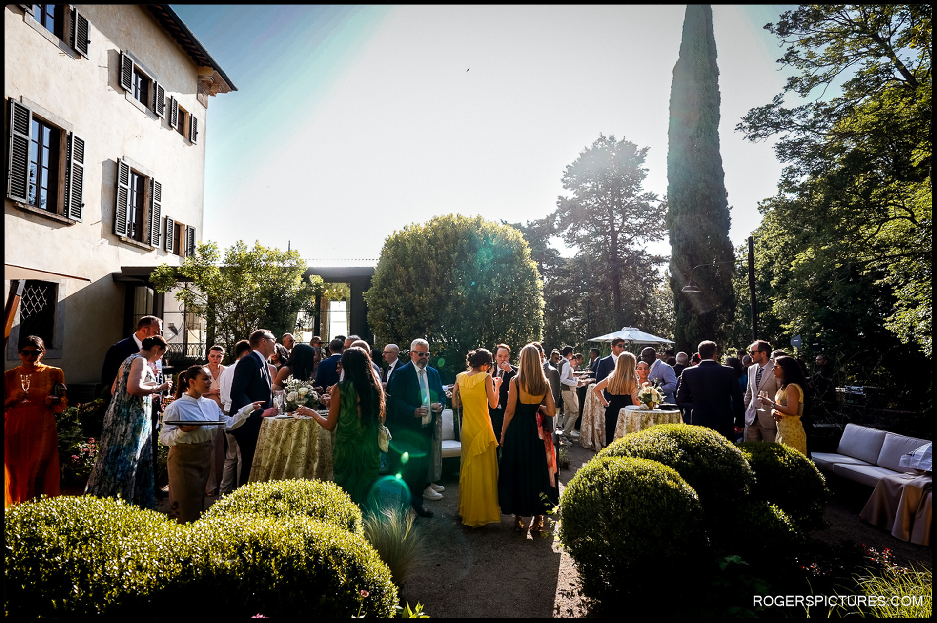 Wedding guests enjoy an elegant outdoor reception at a Tuscan villa surrounded by lush gardens.