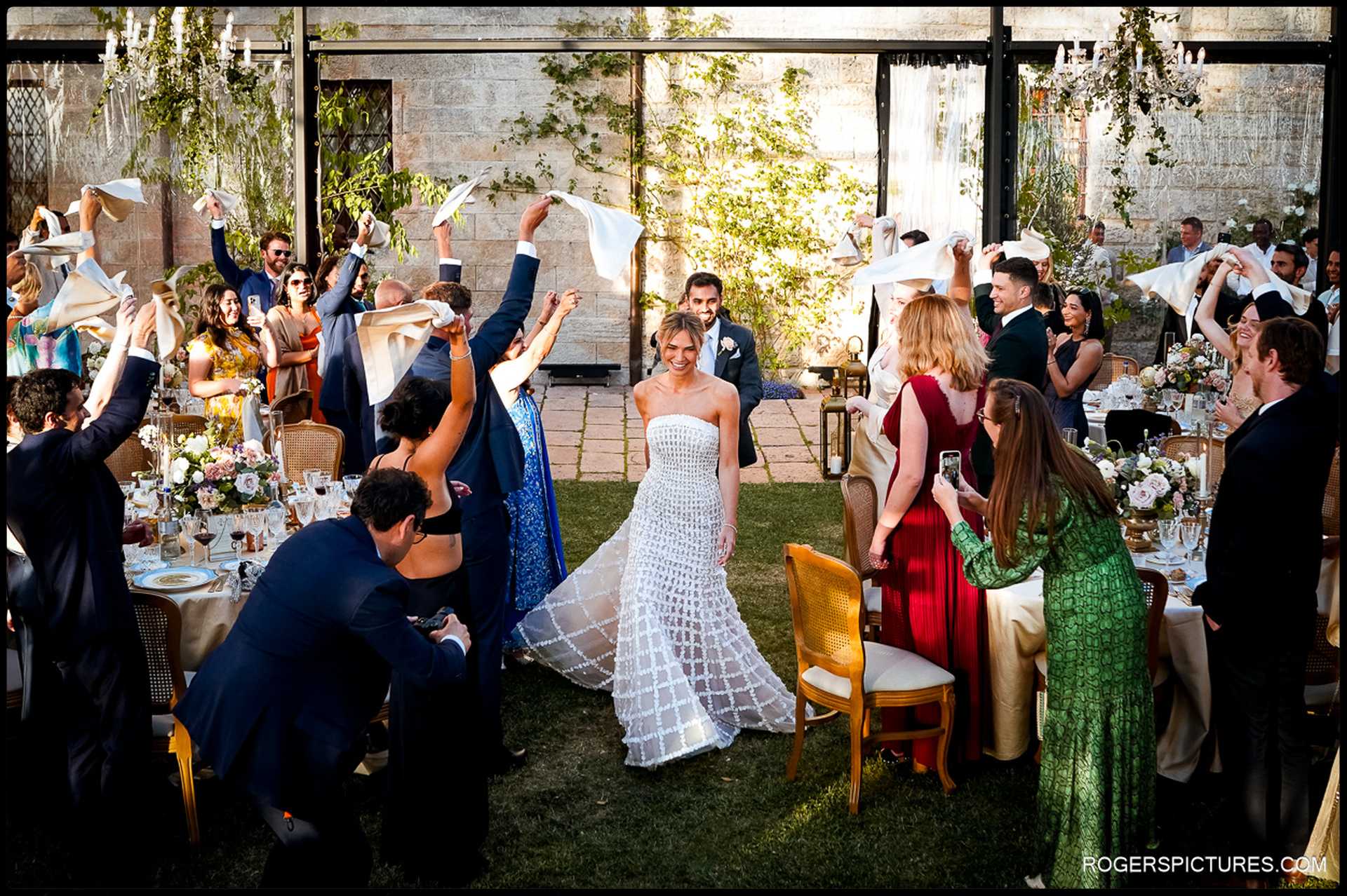 The bride walks through an aisle of waving napkins at her Tuscany woodland wedding reception.