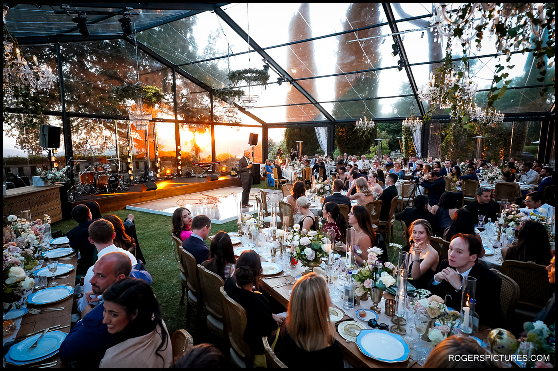 A golden sunset illuminates the elegant Tuscany wedding reception under a transparent marquee.