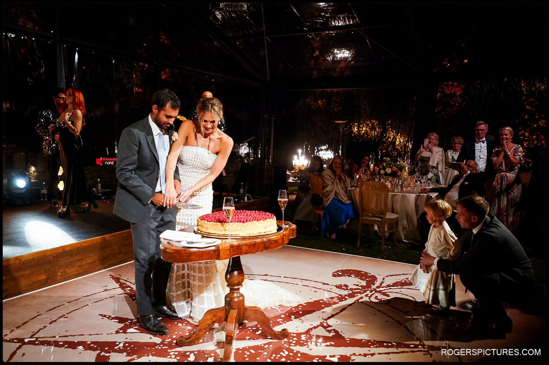 The couple cuts into a rustic berry tart wedding cake, surrounded by delighted guests.