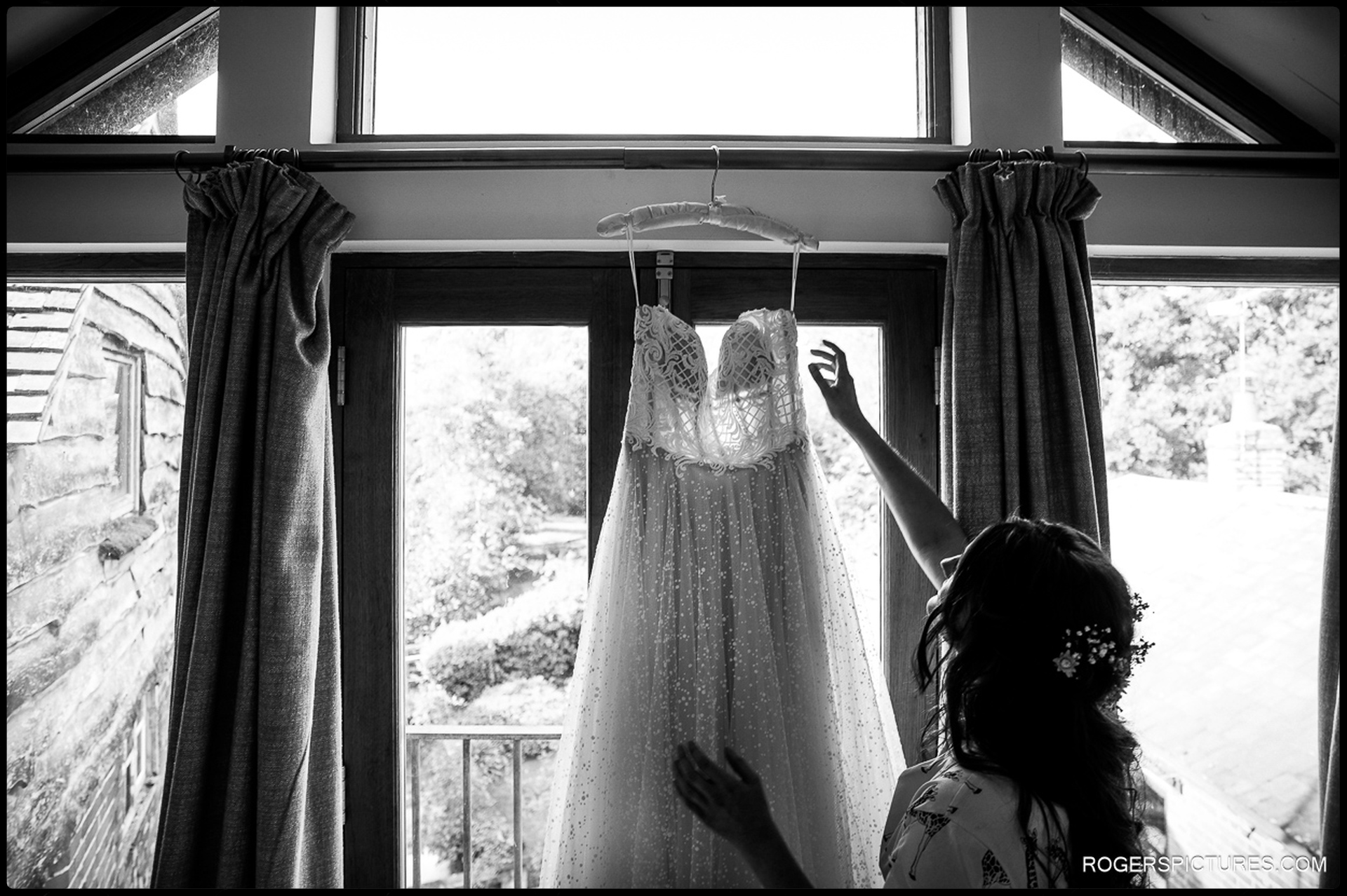 Black and white photo of a bride reaching for her wedding dress