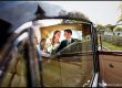 Bride and groom smiling at each other in the back of a vintage car on their way to a marquee wedding party in Essex.