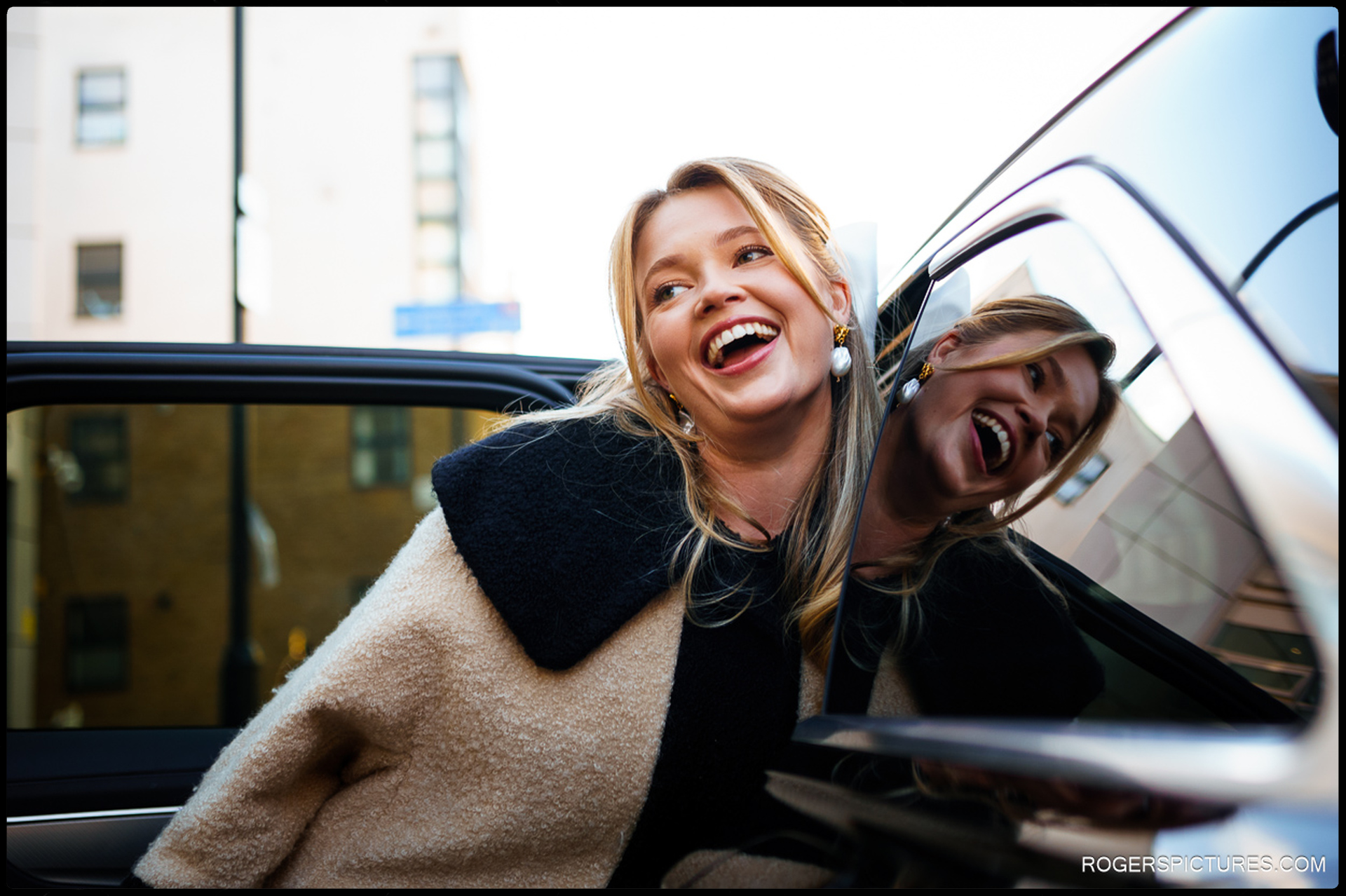Bride laughing as she arrives for her Short Wedding at Hackney Town Hall, reflected in the car window.