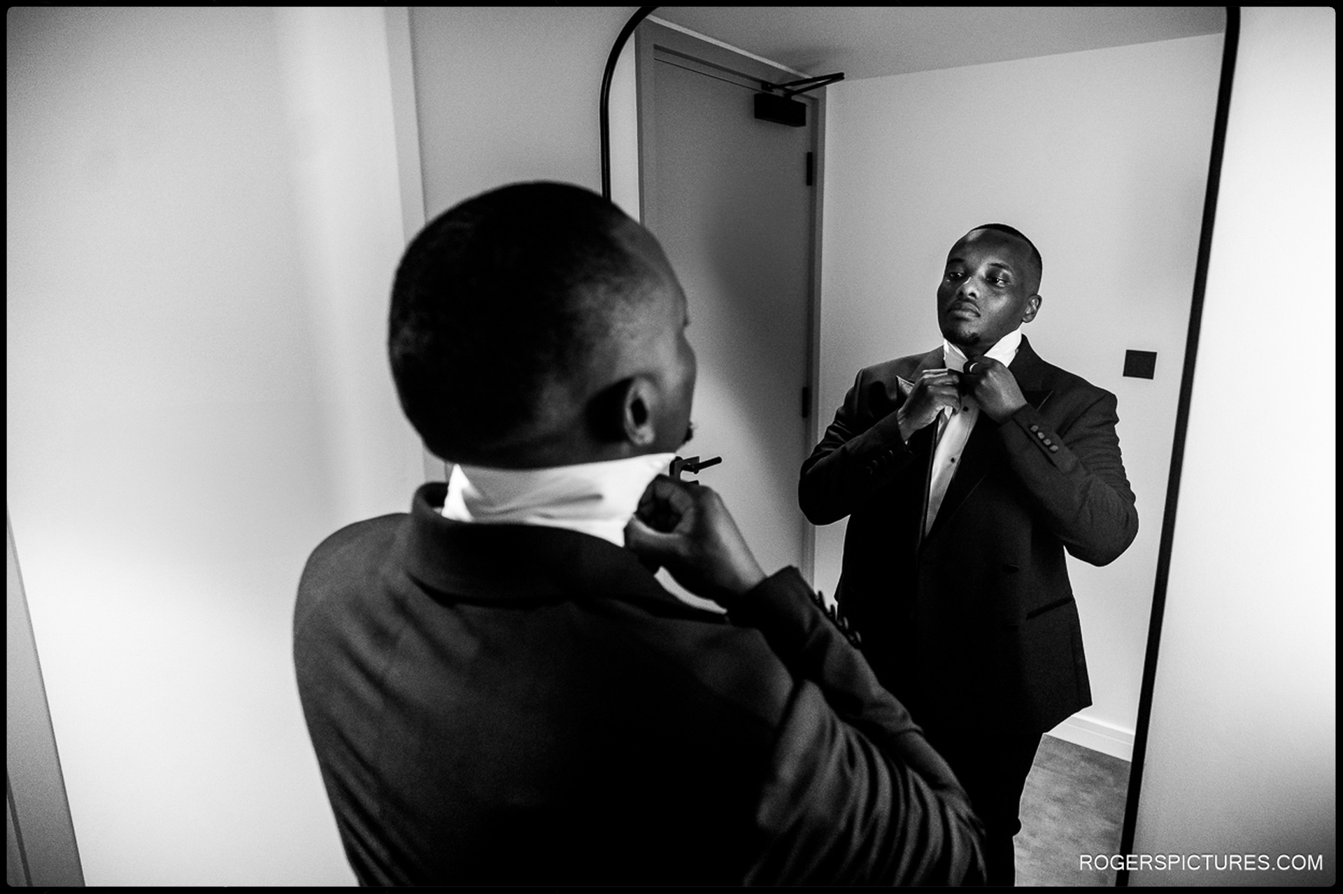 Groom adjusting bow tie in front of mirror at Southgate Hotel, North London