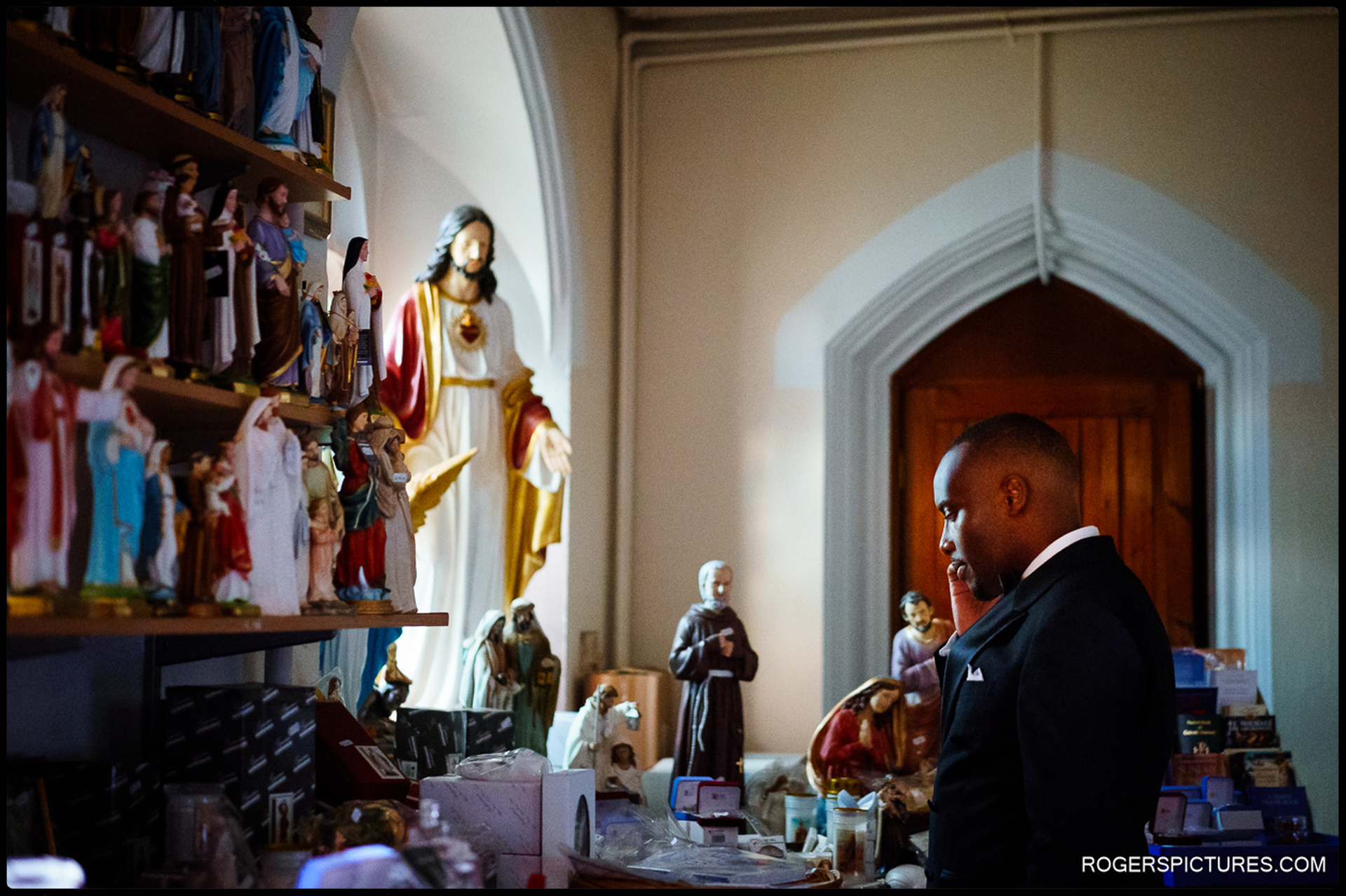 Groom in quiet reflection surrounded by religious icons before Catholic ceremony