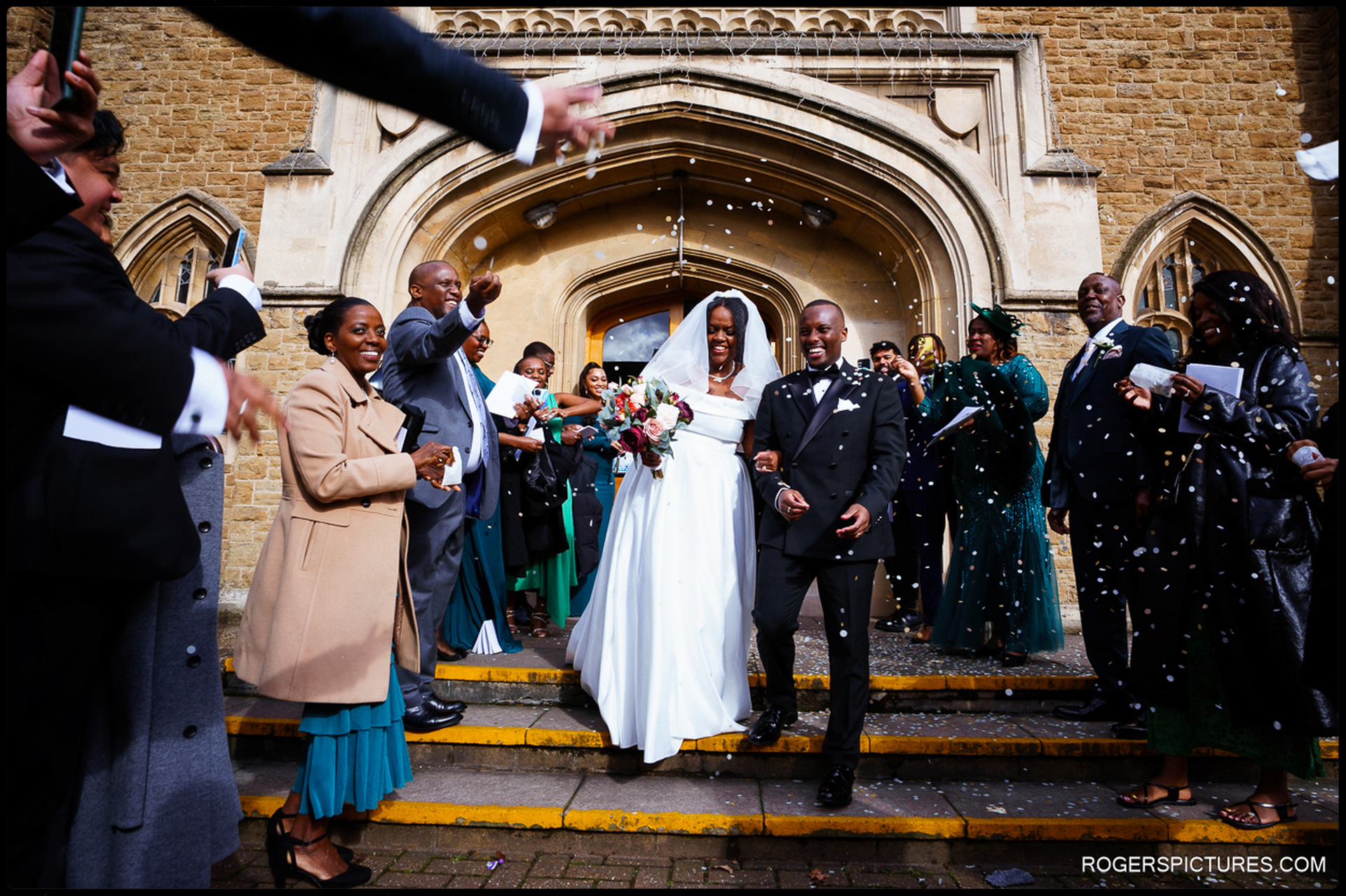 Newlyweds surrounded by guests throwing confetti after Catholic wedding ceremony
