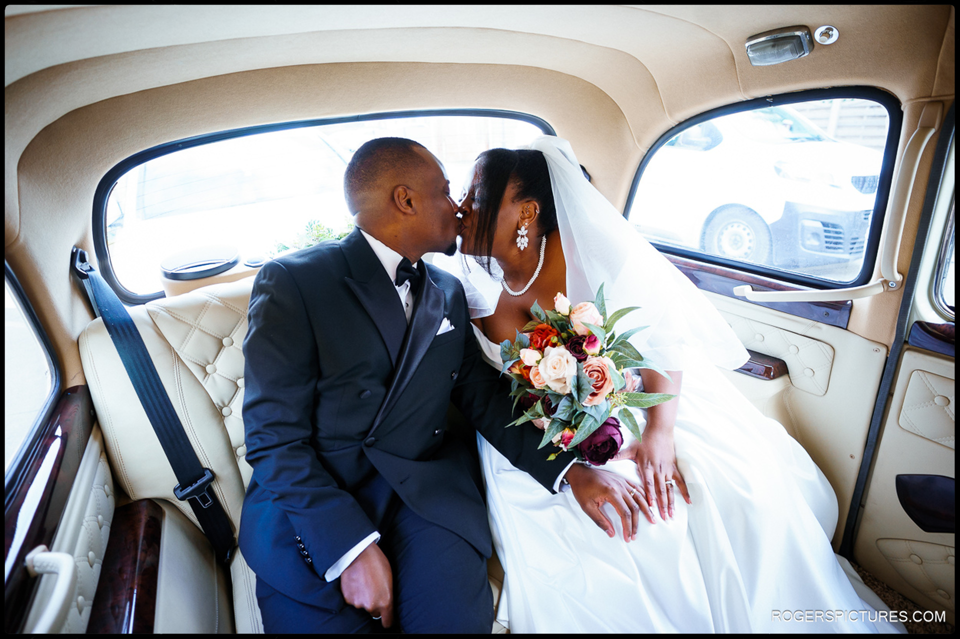 Bride and groom sharing a kiss in the back of a white London taxi after church ceremony