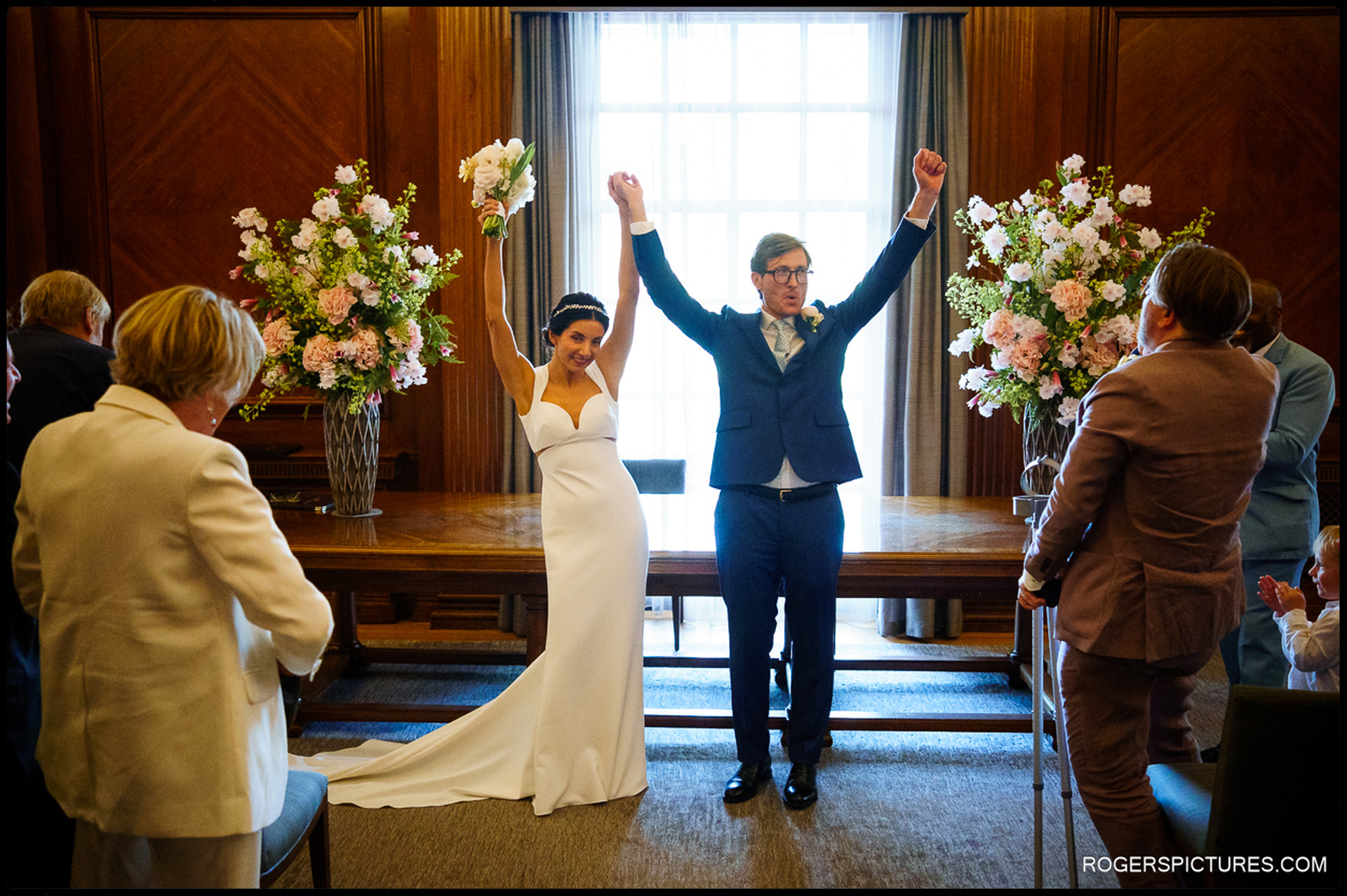 The bride and groom celebrate with raised hands after exchanging vows at Marylebone Town Hall.
