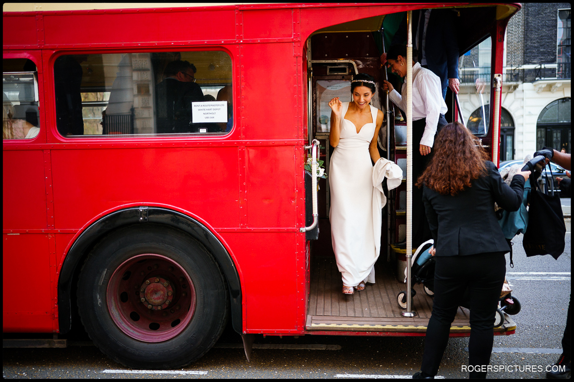 The bride waving as she steps off the vintage red Routemaster bus in London.