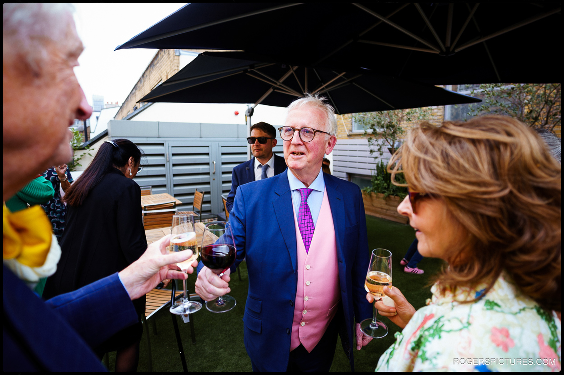 A cheerful toast on the rooftop terrace at 41 Portland Place, with guests celebrating under large umbrellas.