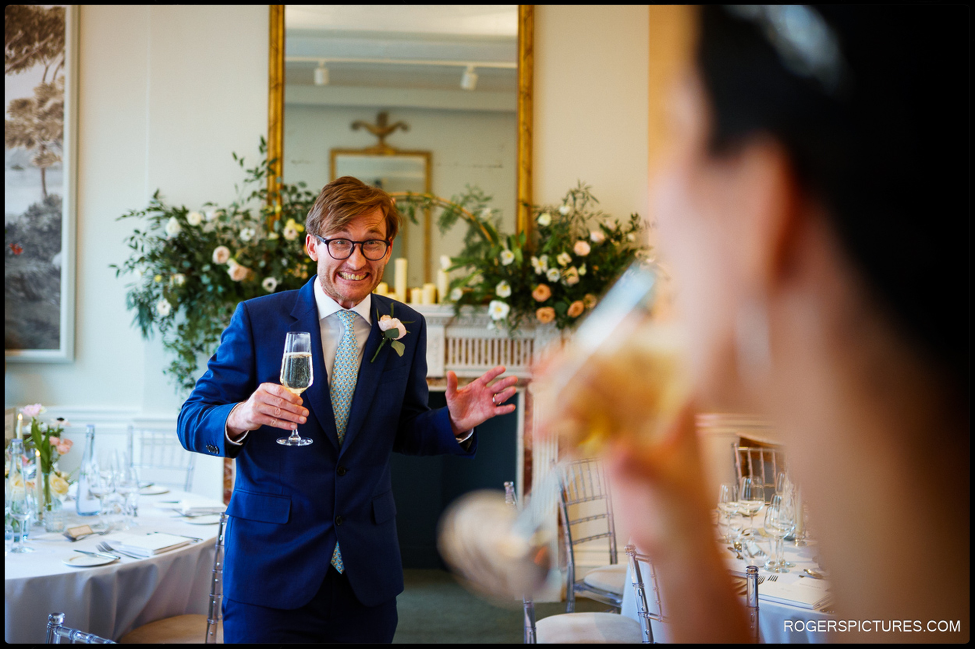 The groom enthusiastically raising a glass during the wedding reception inside 41 Portland Place, surrounded by elegant floral decorations.