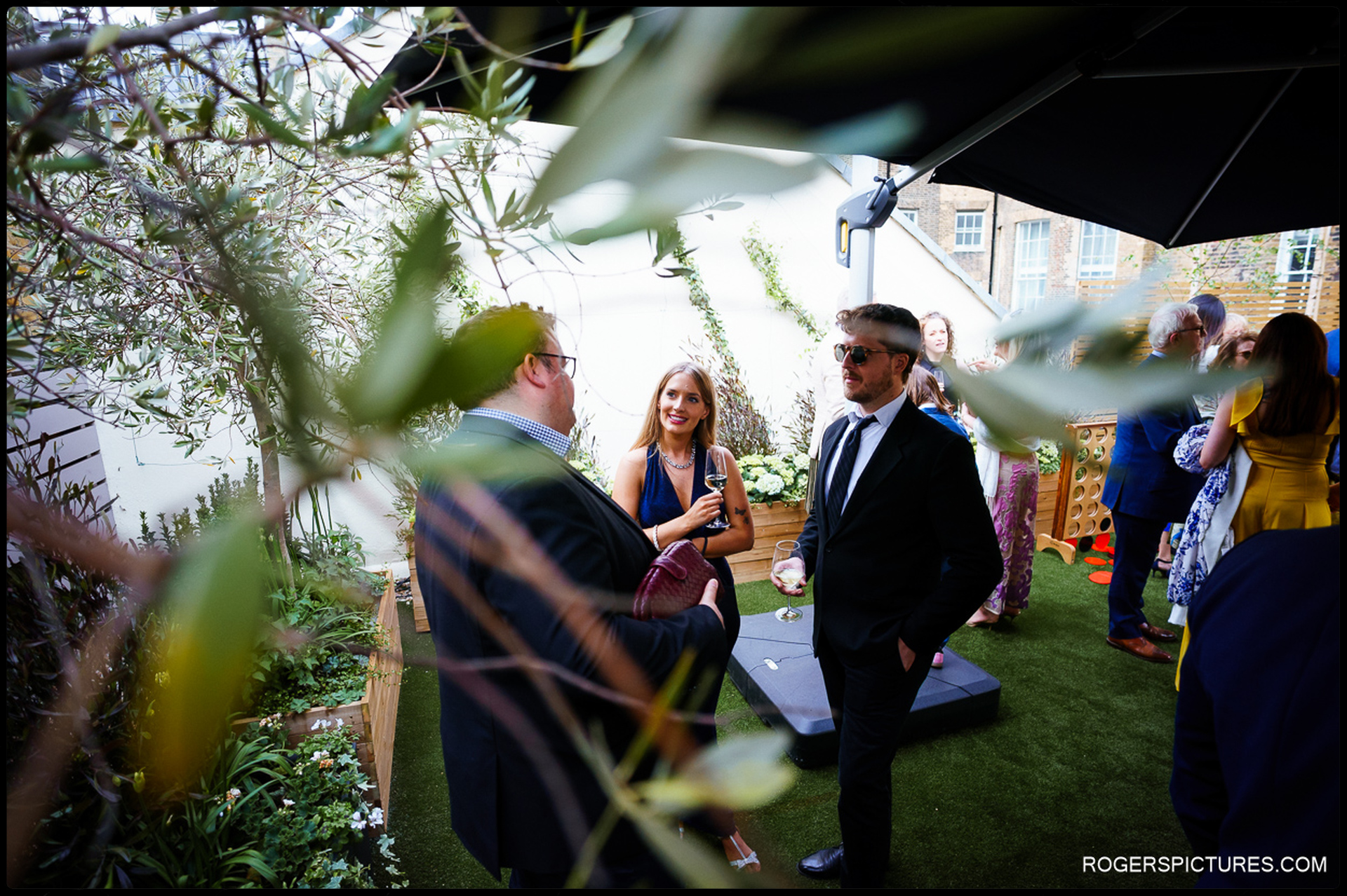 Guests mingling beneath olive branches on the rooftop terrace at 41 Portland Place during the wedding reception.