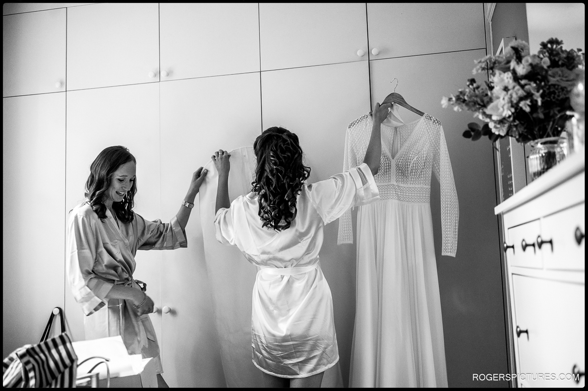 Bride and bridesmaid admiring the wedding dress hanging on a wardrobe.