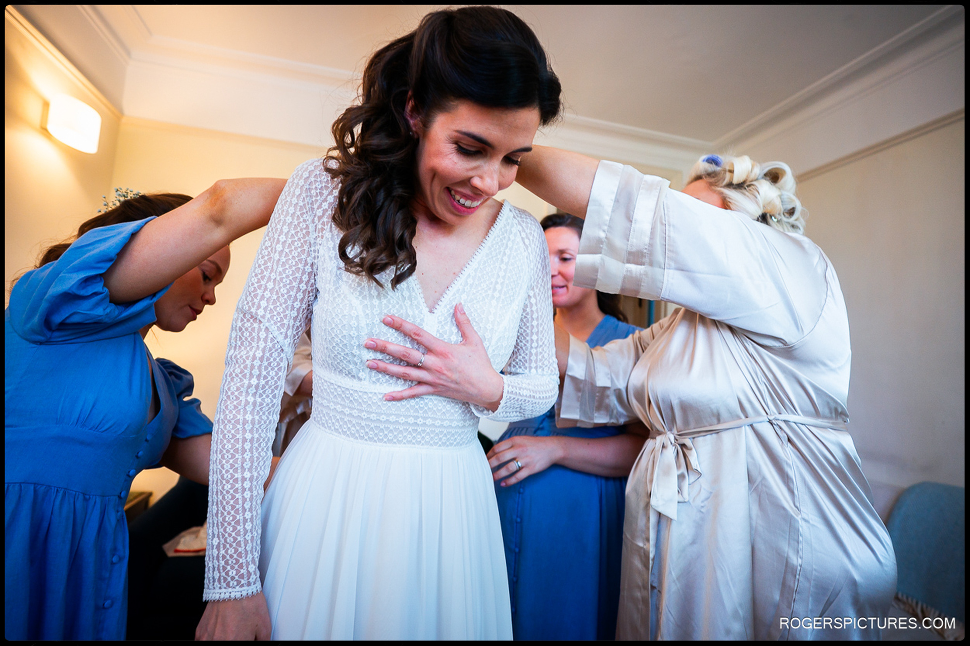 Bridesmaids helping bride into her wedding dress.