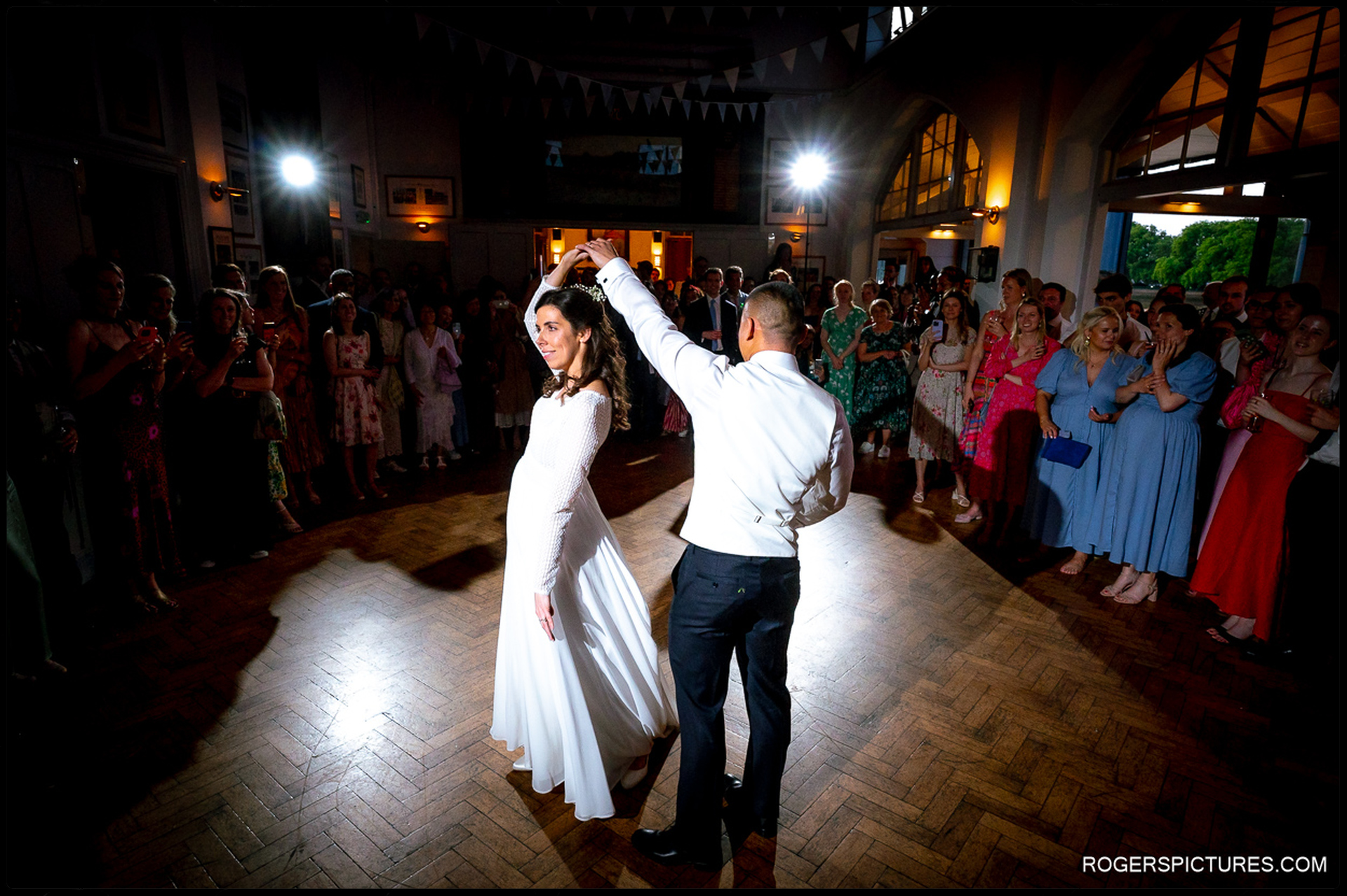 Bride and groom sharing their first dance under spotlights as guests gather to watch.