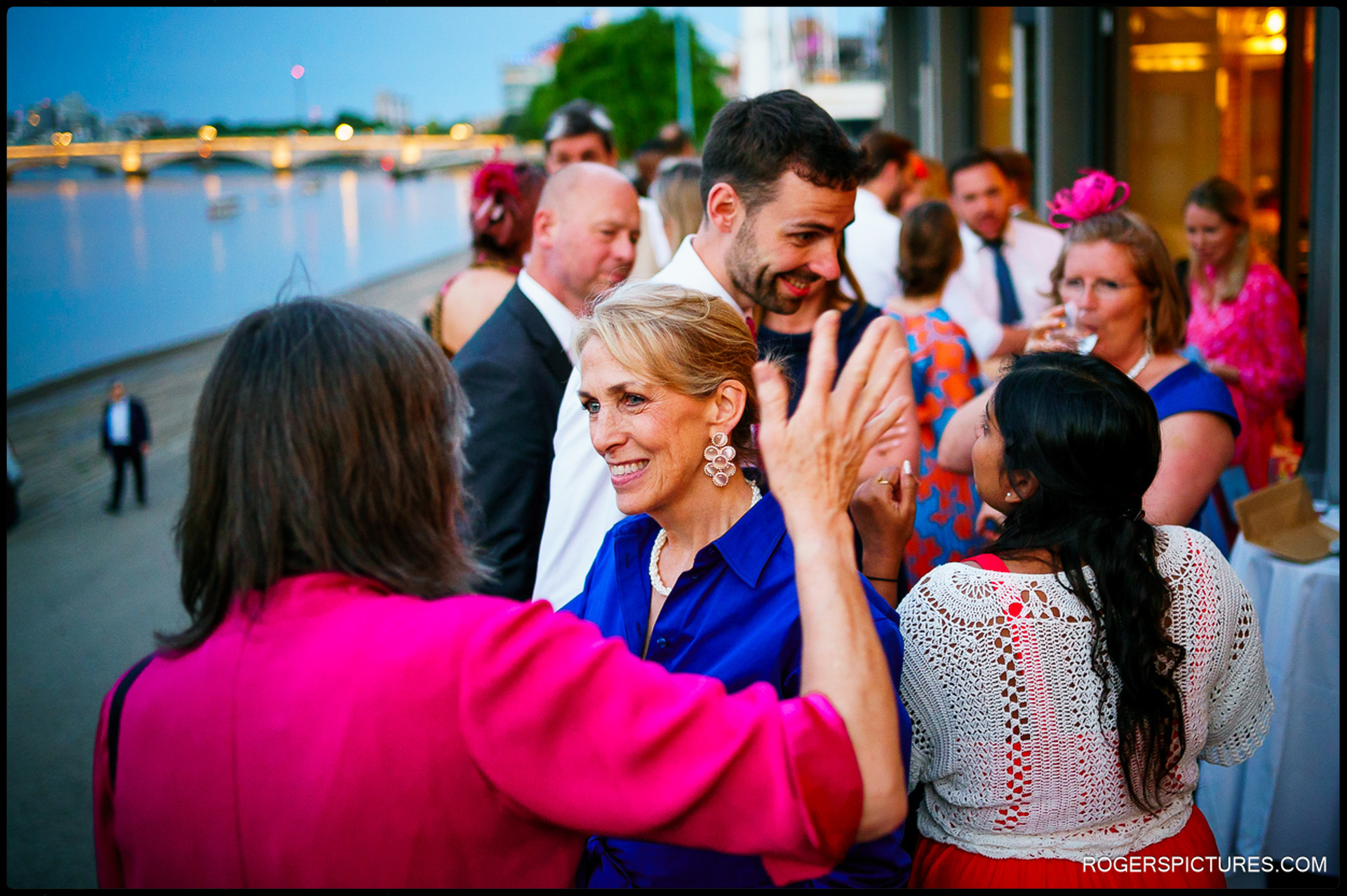 Wedding guests chatting and laughing outside Thames Rowing Club by the river