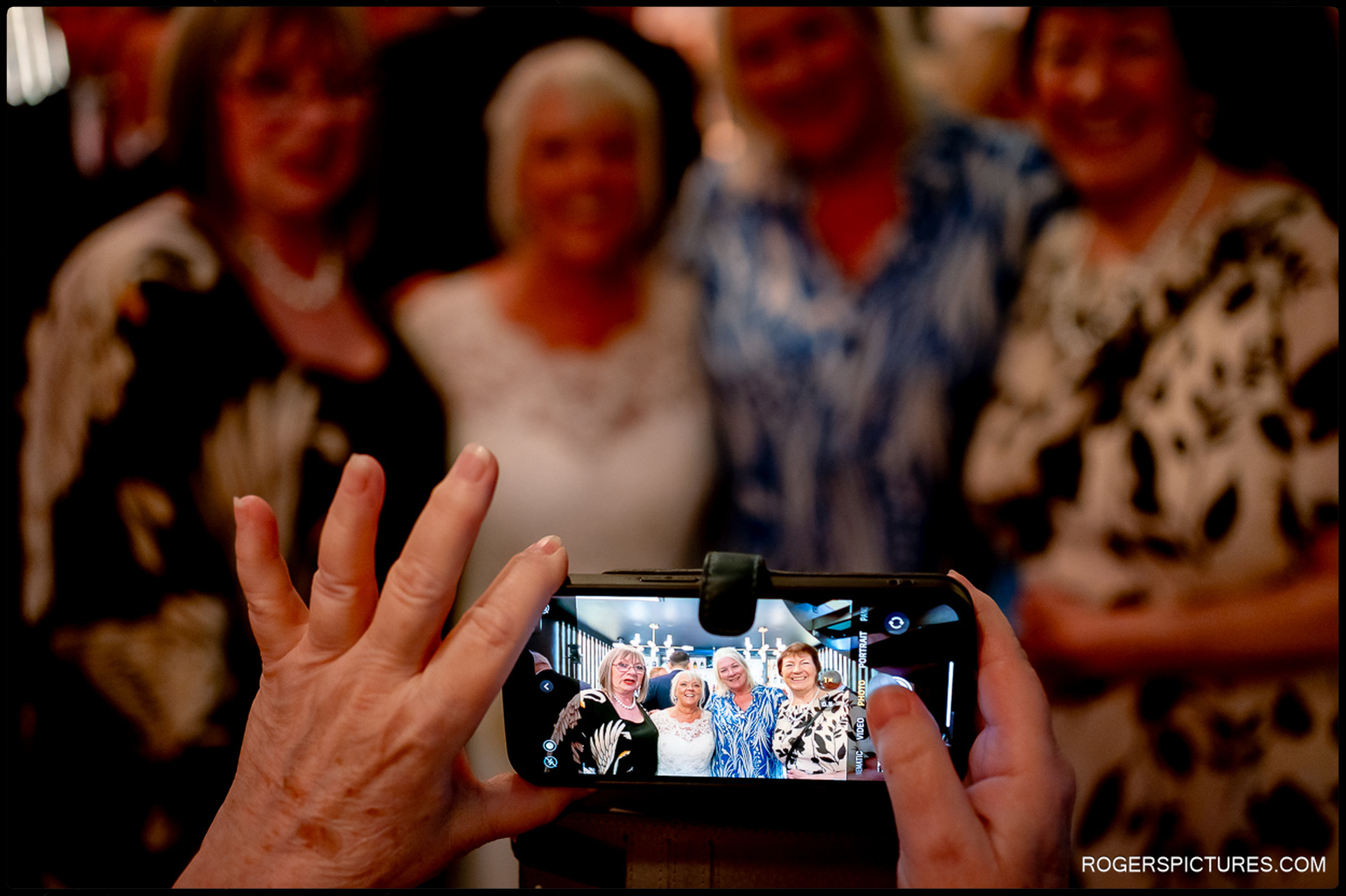 Smartphone captures a group portrait of the bride and three women posing inside the venue.