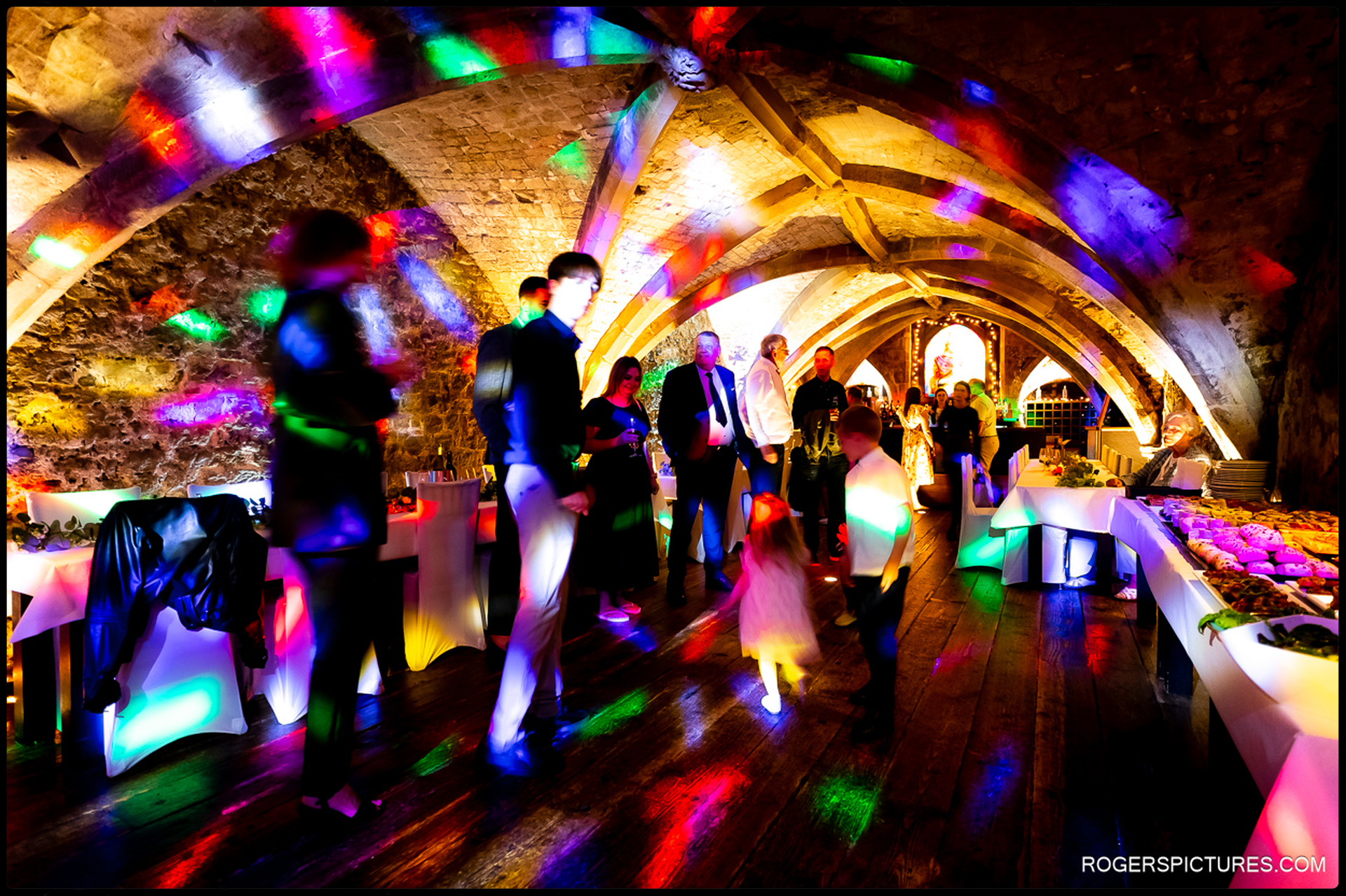 Colourful disco lights illuminate wedding guests dancing in the arched stone cellar of the George Vaults.