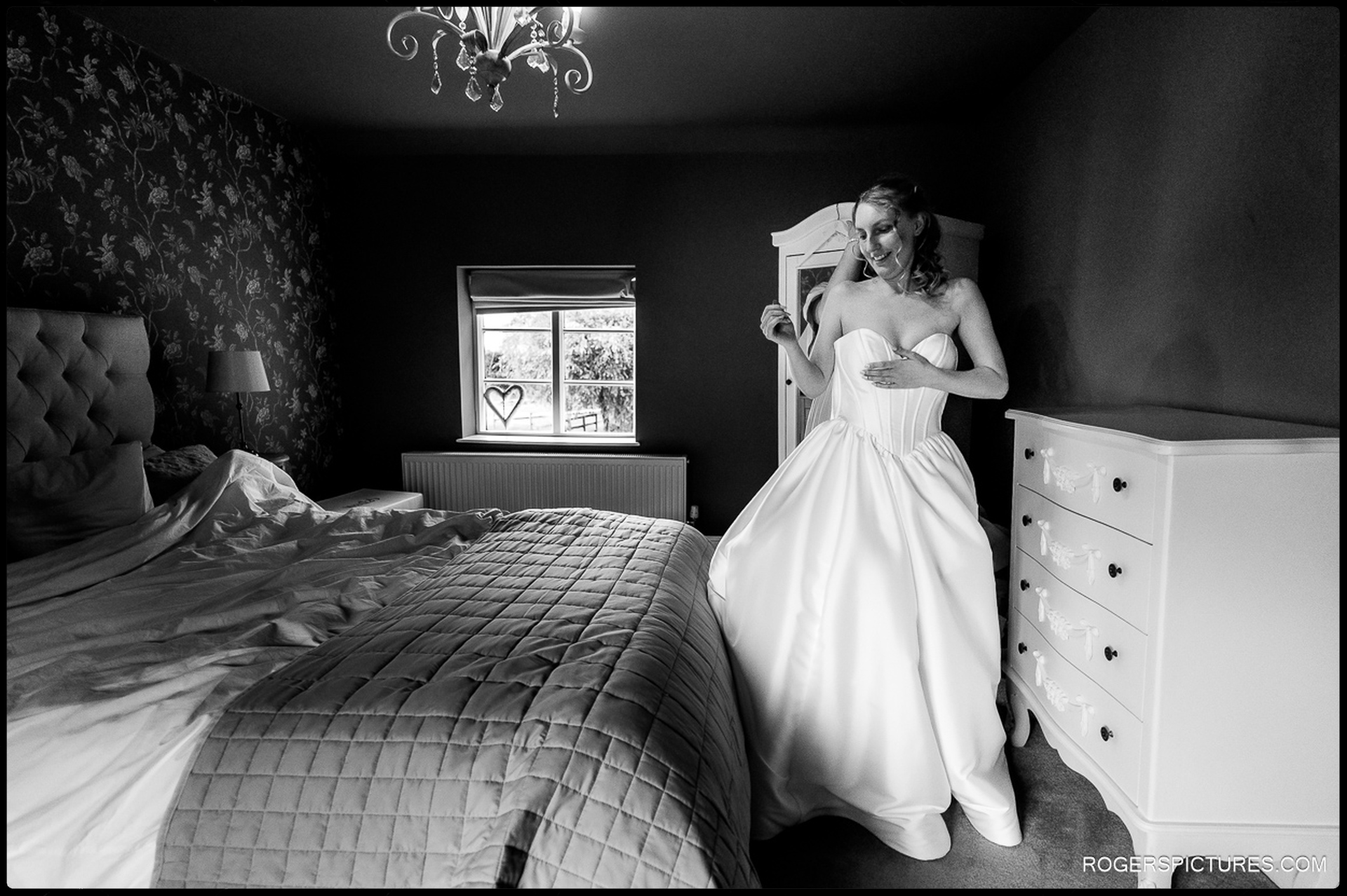 Bride adjusting her wedding dress in a softly lit bedroom before leaving for the ceremony.