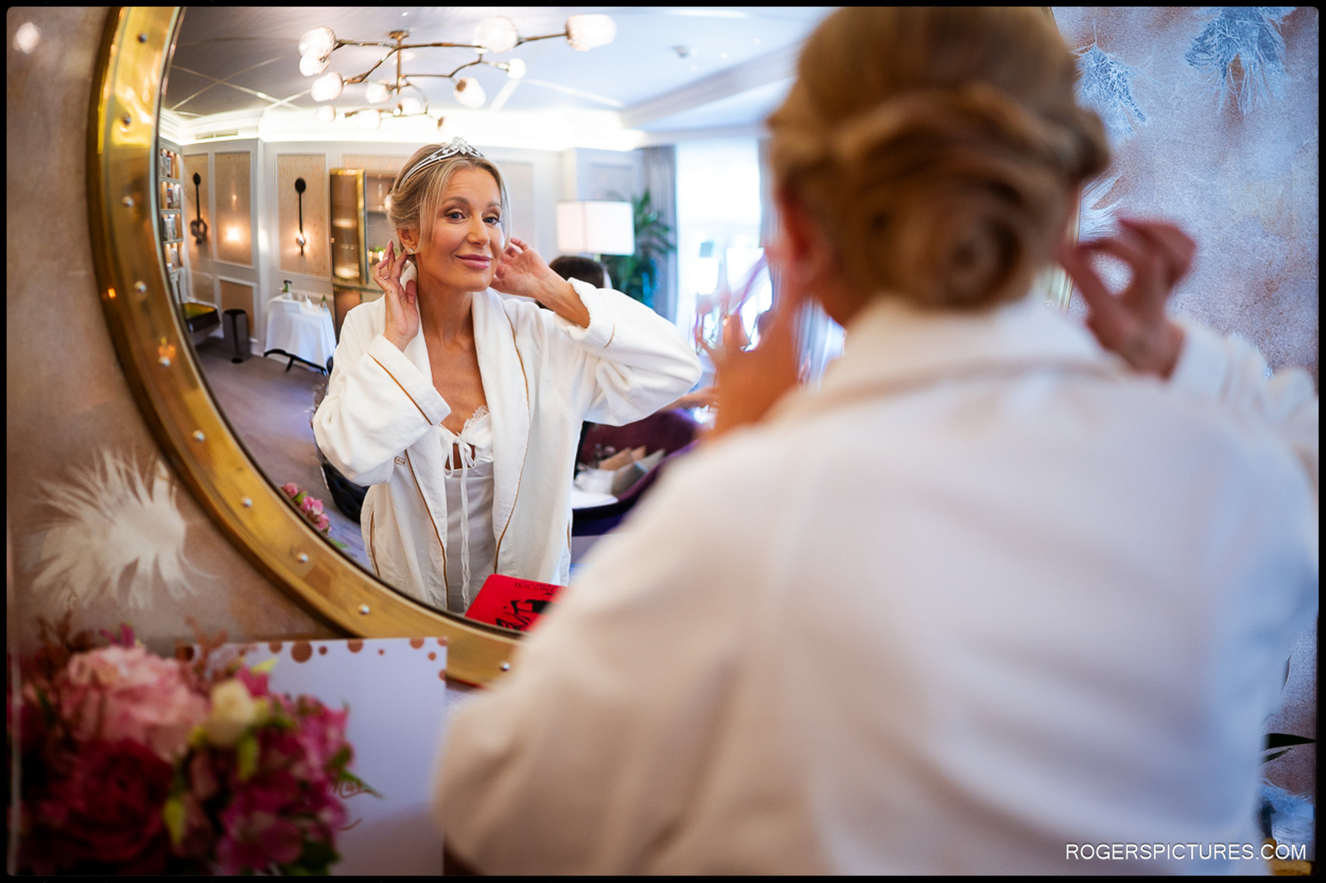 Bride adjusting her earrings in front of a mirror while getting ready at the Mandarin Oriental in Knightsbridge, reflected in the room’s warm light.