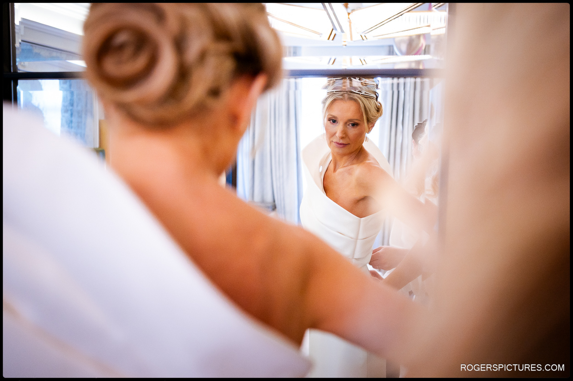 Bride looking into the mirror as she adjusts her dress, captured in a quiet moment before leaving for the ceremony.