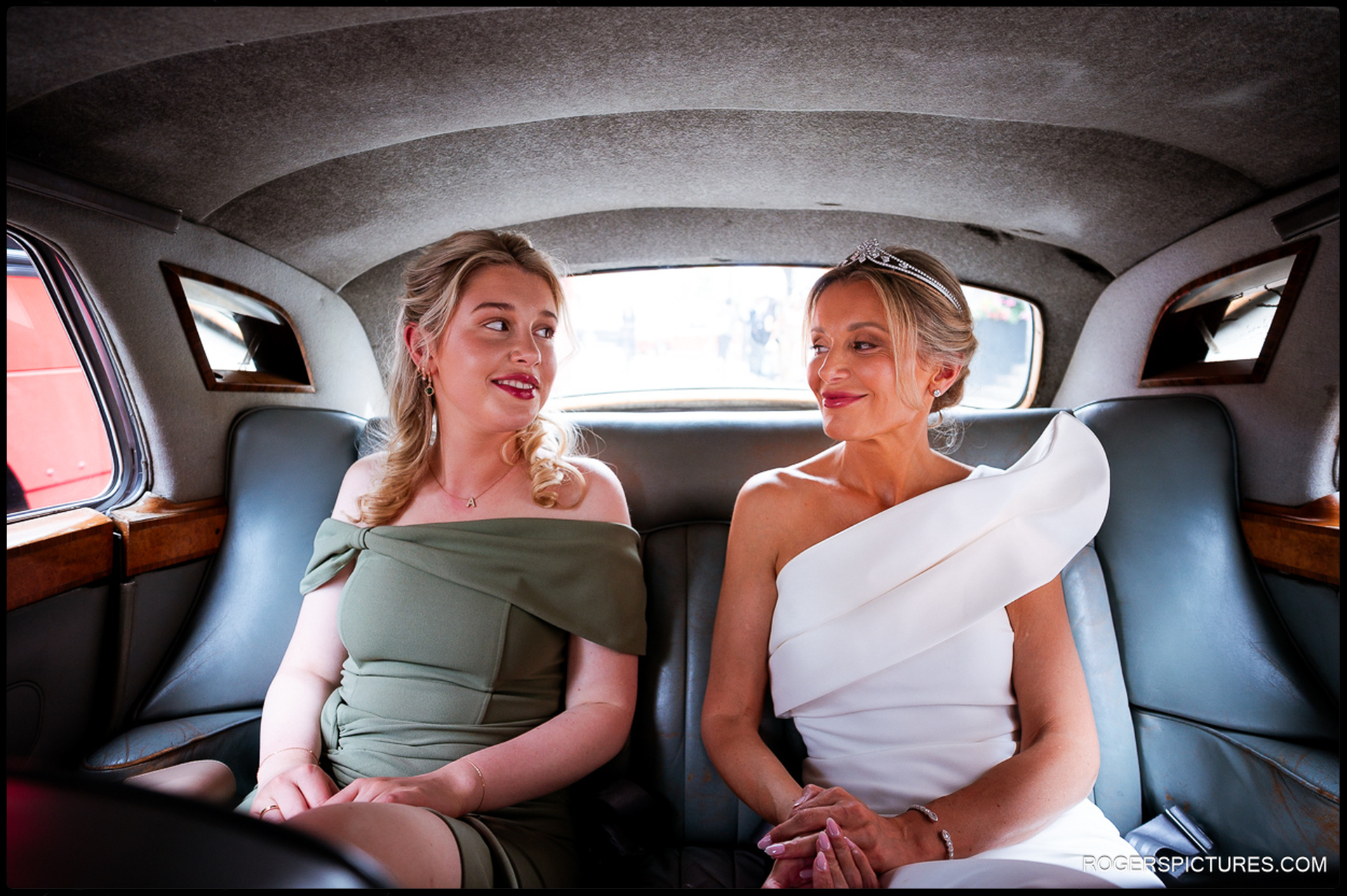 Bride and bridesmaid sitting together in the back of a vintage car, sharing a calm and happy moment on the way to the ceremony.