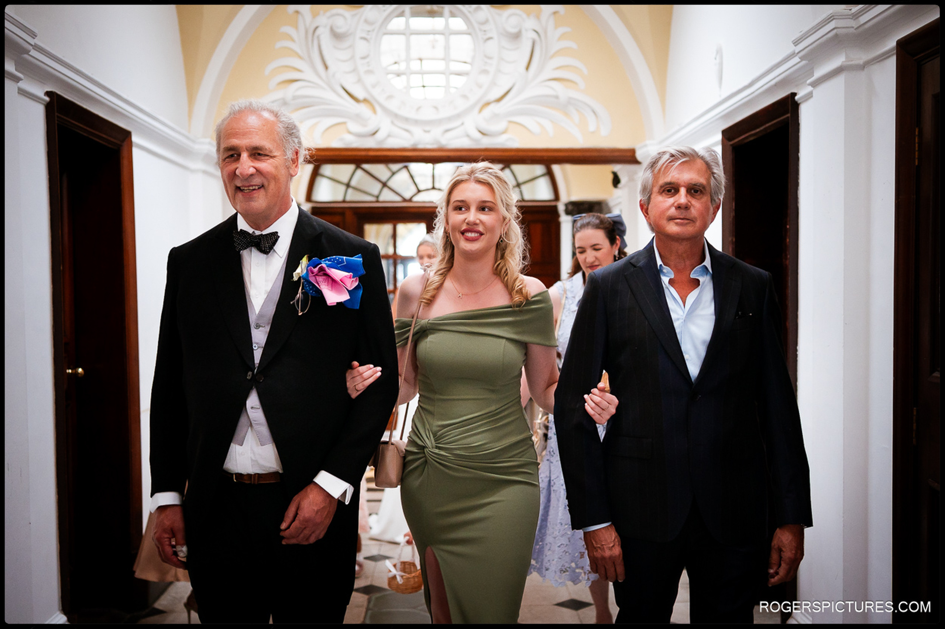 Guests walking down the elegant hallway at Chelsea Old Town Hall, led by a bridesmaid in a green dress and family members in formal wear.