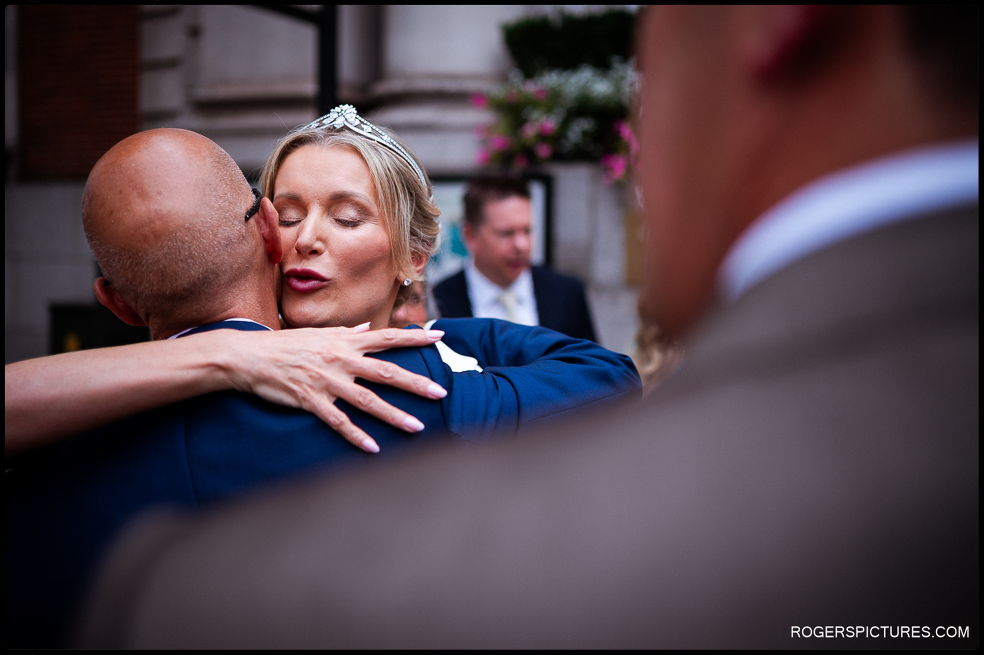 Bride embracing a guest warmly outside Chelsea Old Town Hall, eyes closed in a candid moment of affection.