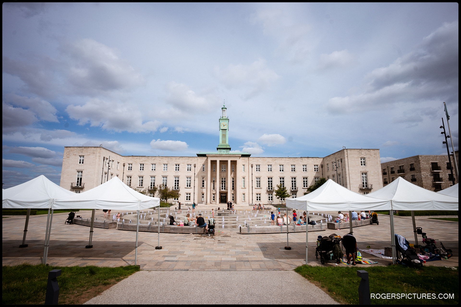 Wide view of Waltham Forest Town Hall and Fellowship Square on a sunny summer day, with fountains, families enjoying the space and white canopies set up in the square.