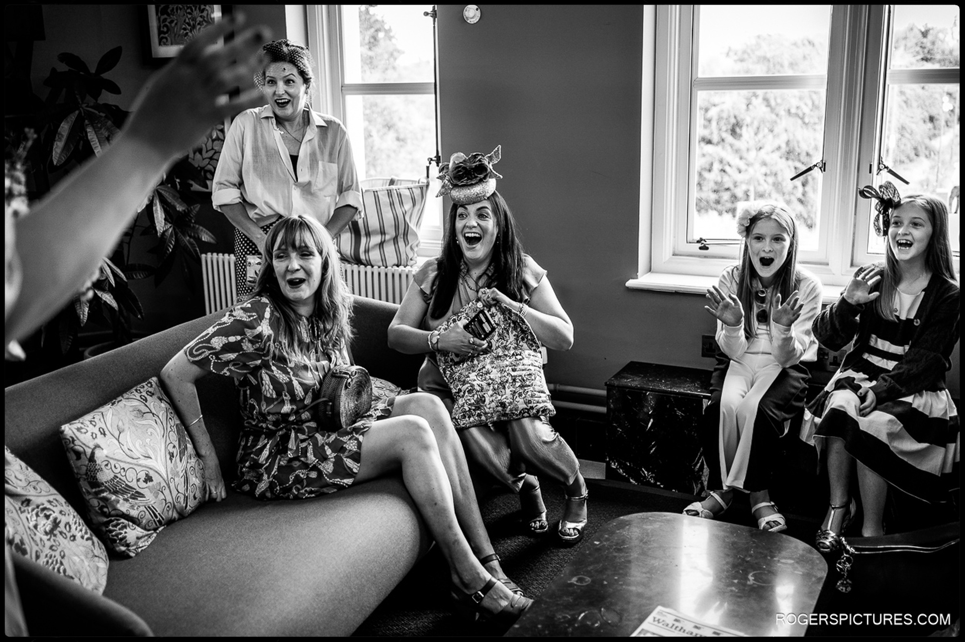 Wedding guests laughing and reacting with excitement while waiting inside Waltham Forest Town Hall before the ceremony, captured in candid black-and-white documentary style.