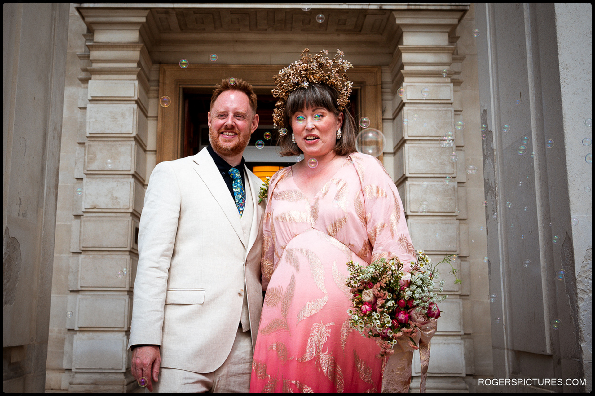Newly married couple standing on the steps of Waltham Forest Town Hall surrounded by bubbles, smiling after the ceremony.