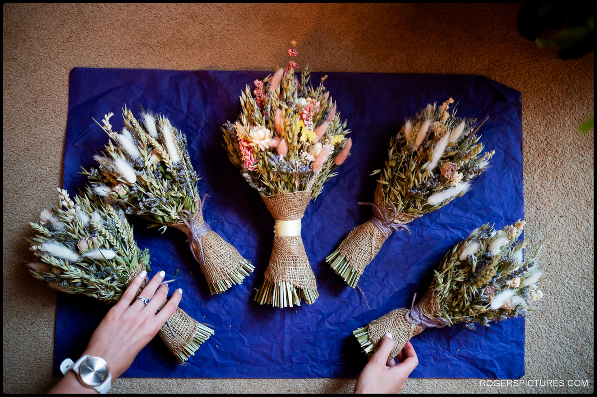 Rustic dried flower bouquets laid out on deep blue tissue paper, hands arranging them.