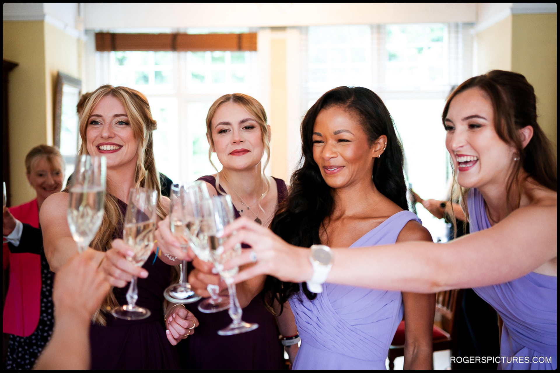 Bridesmaids clinking champagne glasses together with joyful expressions during getting-ready celebrations.
