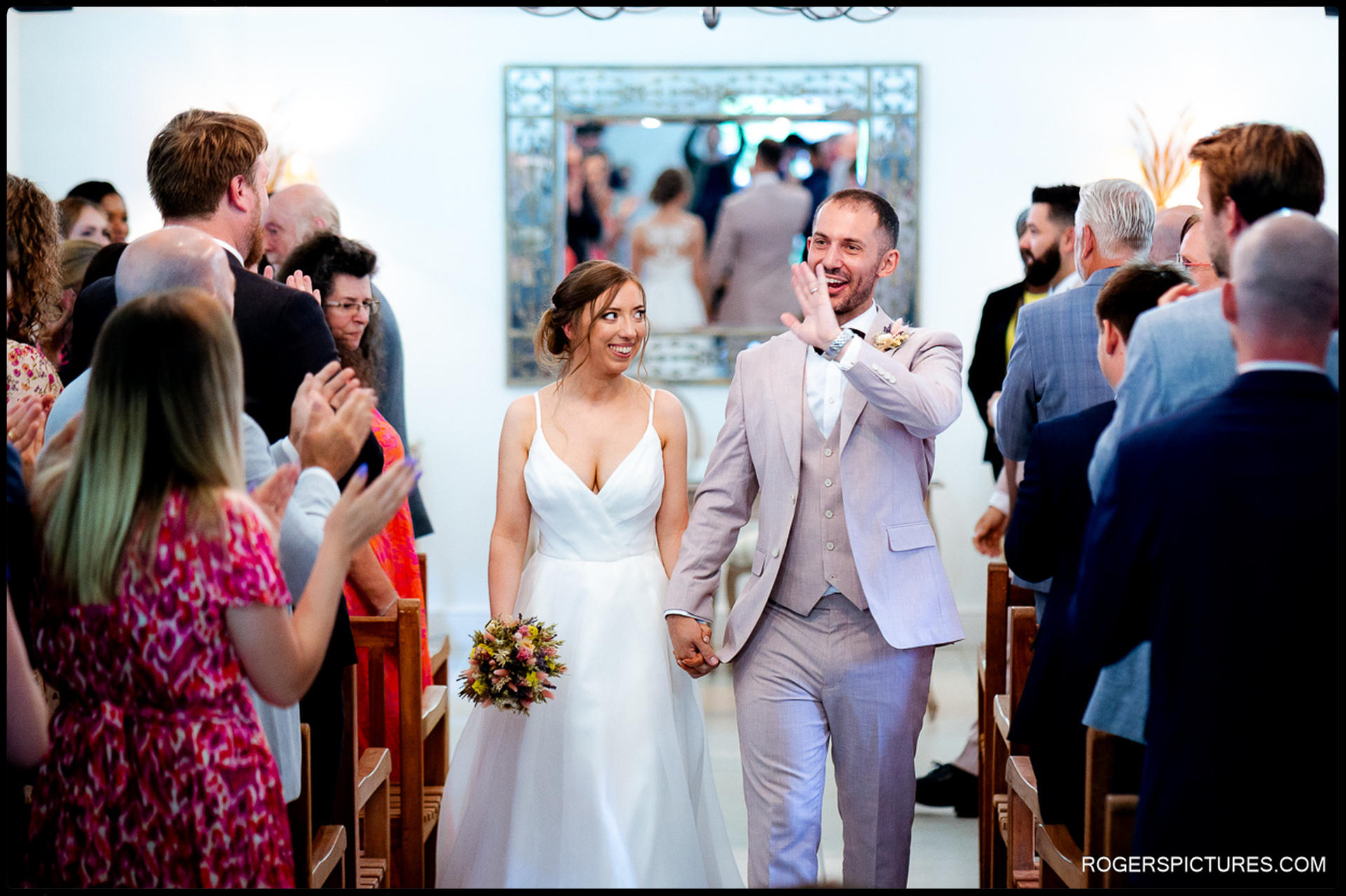 Bride and groom walking back up the aisle together smiling, guests applauding and cheering around them.