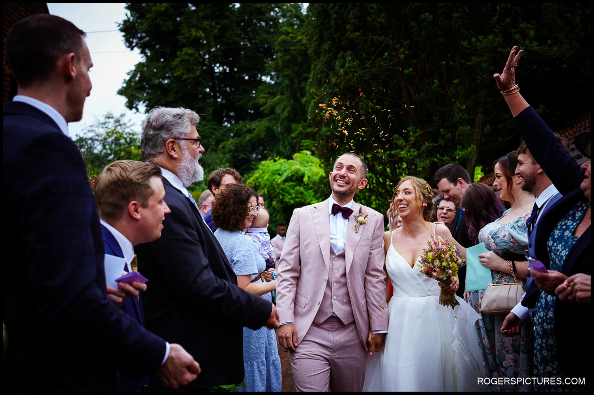 Couple smiling and walking through confetti tunnel as guests throw petals and cheer.