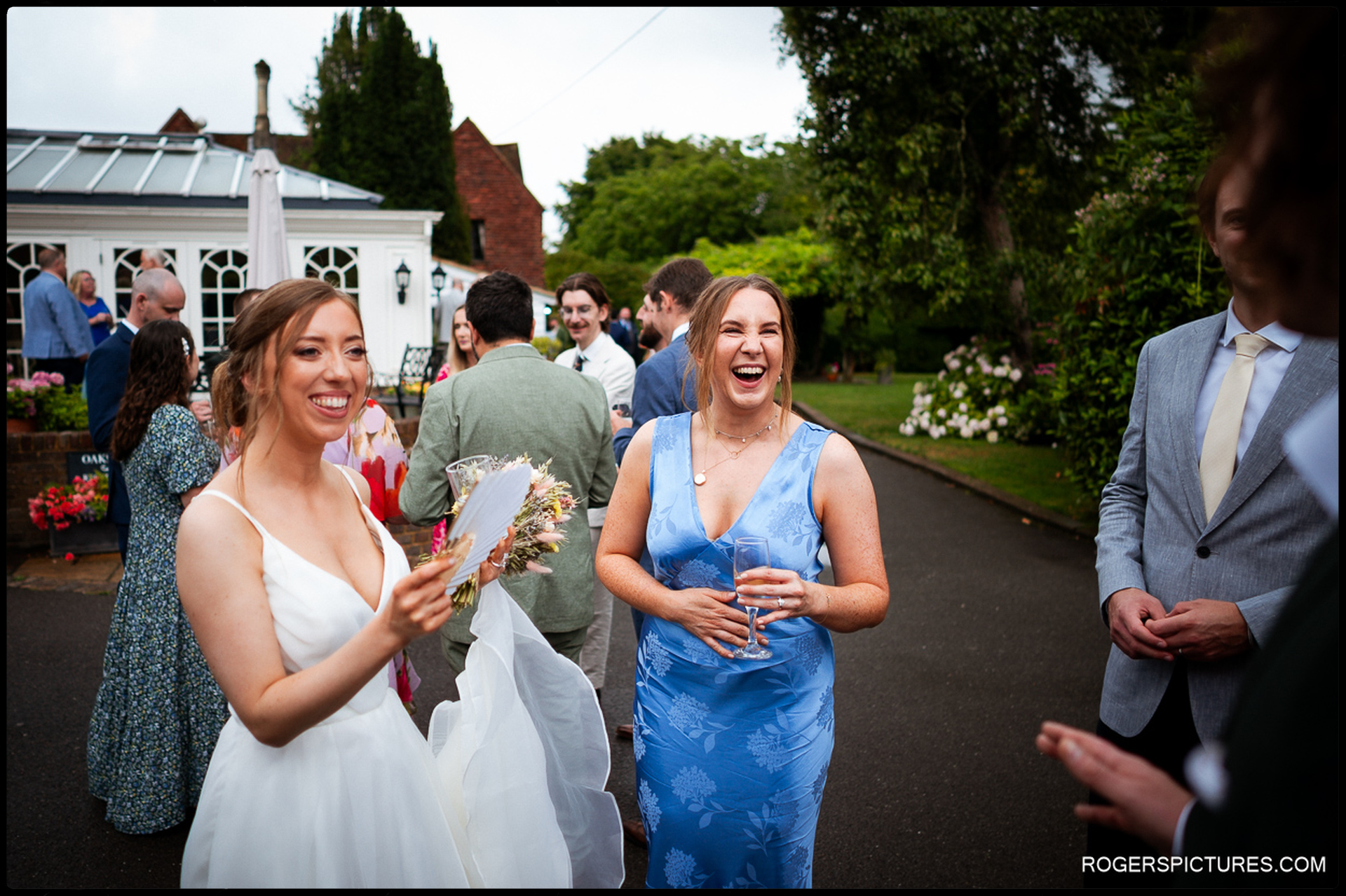 Bride laughing and chatting with guests during drinks reception outside Oaks Farm.