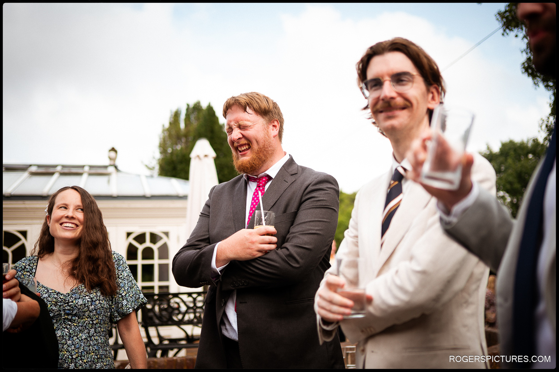 Group of guests laughing and holding drinks during the outdoor reception.