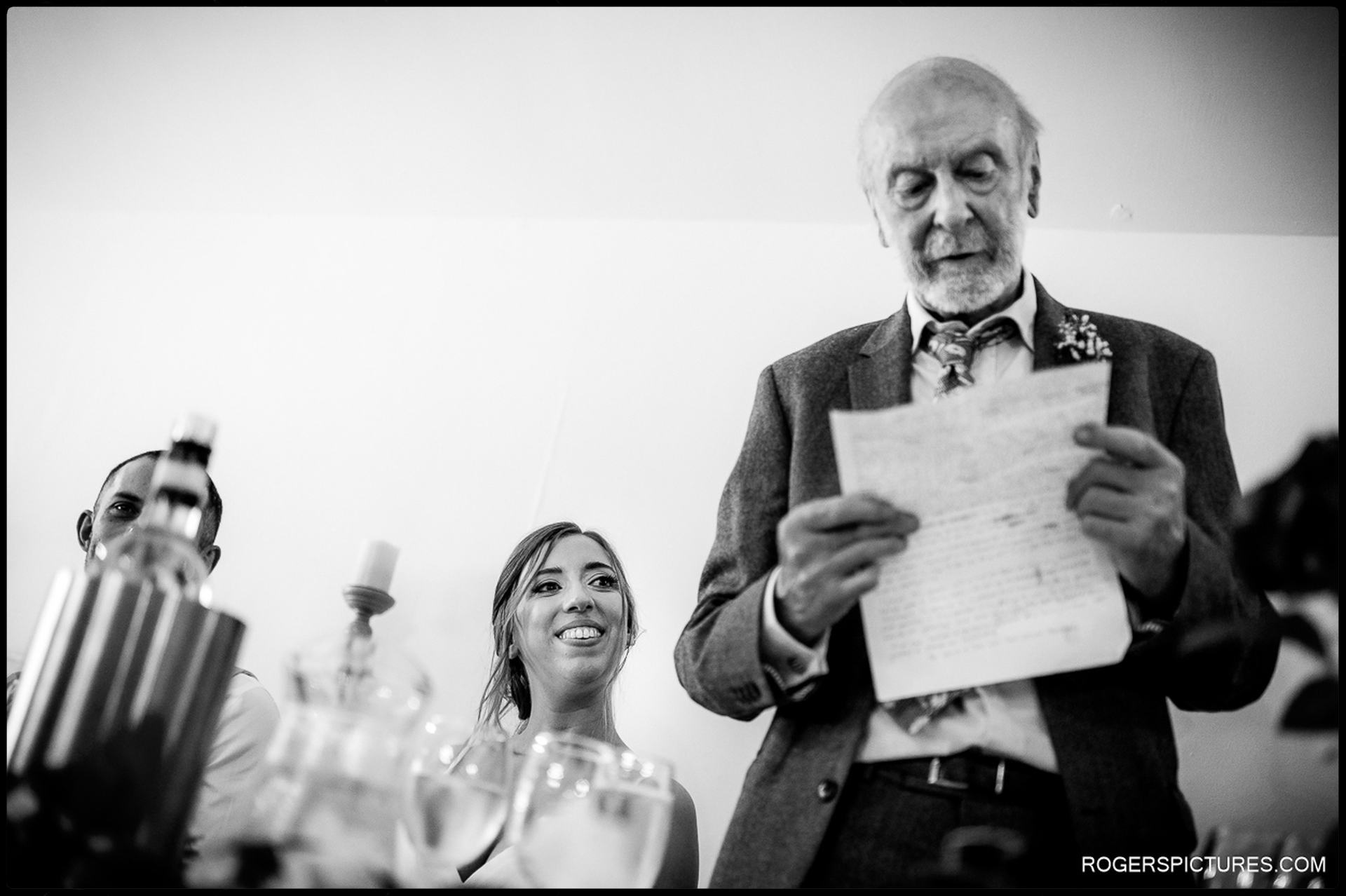 Bride smiling and looking up at her father as he reads a speech at the wedding breakfast.